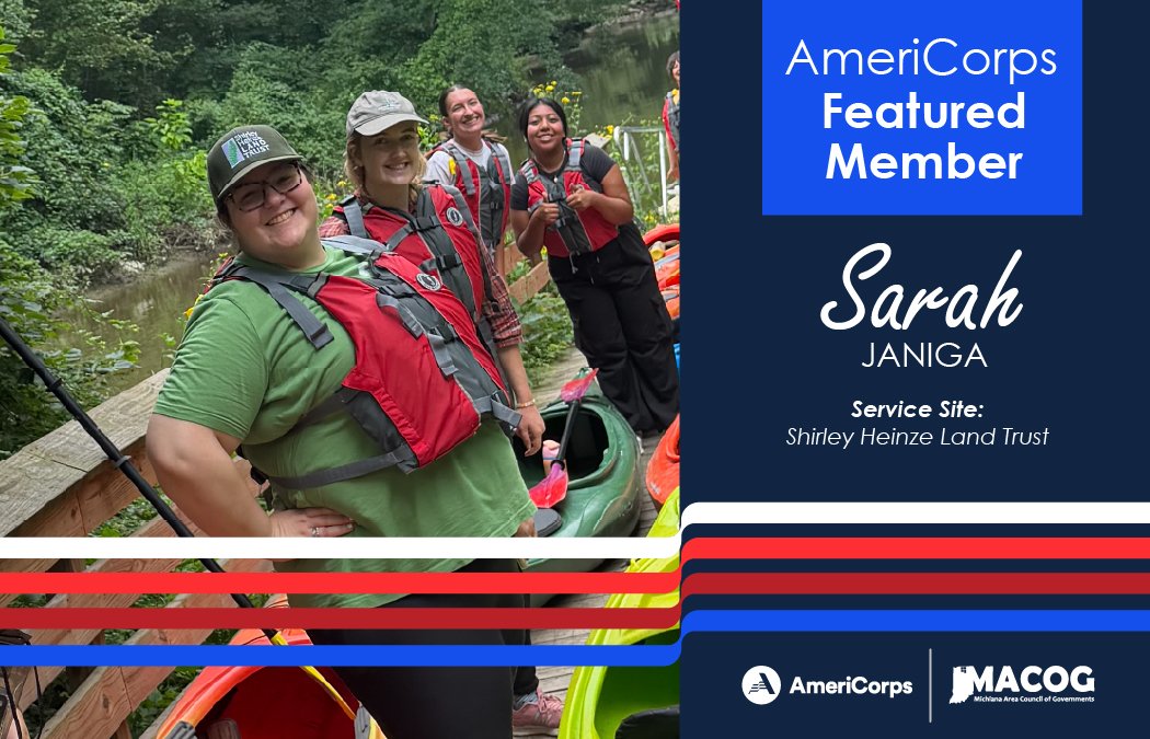 A group of four ladies standing around kayaks with life jackets on. Sarah is in front of the line of girls smiling at the camera.
