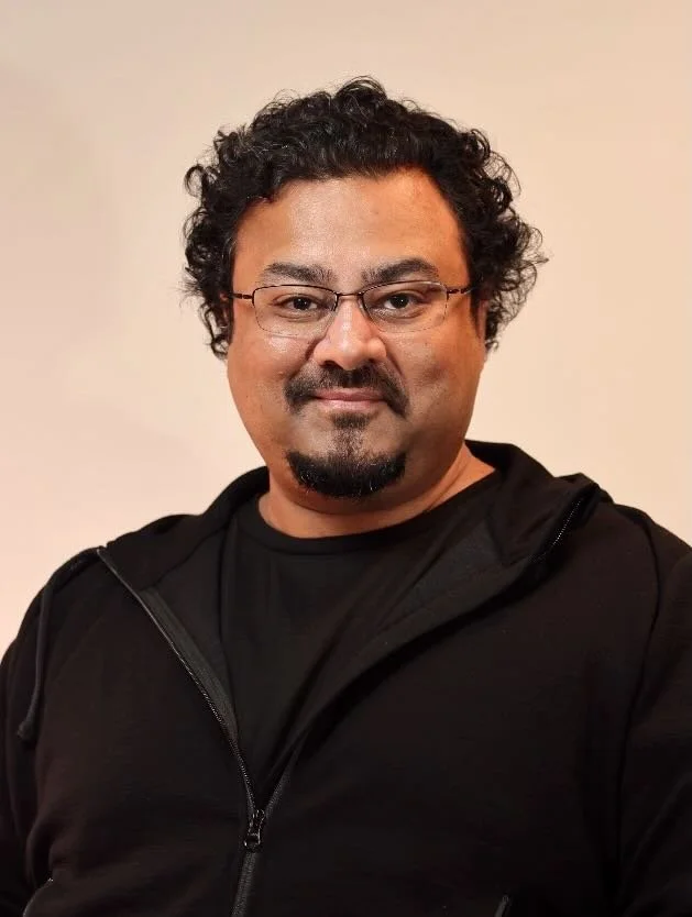 a man with a beard and glasses wearing a black hoodie and a black t-shirt.