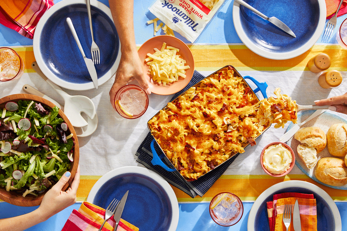 Overhead view of a table set for a meal with mac and cheese, salad, rolls, utensils, napkins, and drinks.