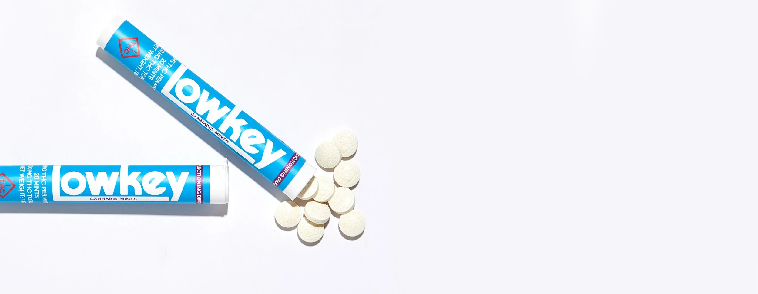 Two tubes of Lowkey Mints low-dose cannabis mints with white tablets spilled on a white surface.