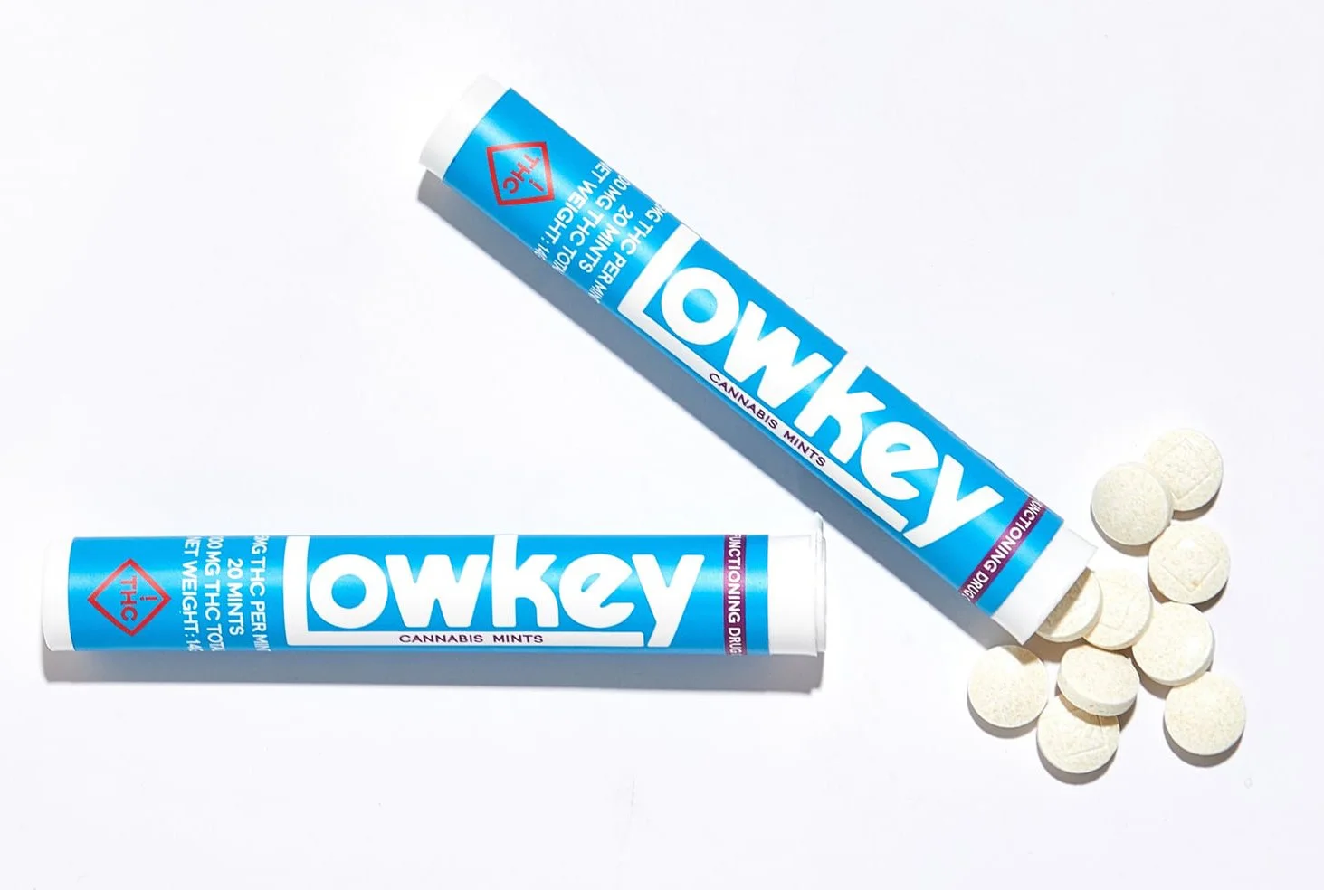 Tube of ow-key cannabis mints with some mints spilled out next to it on a white background.