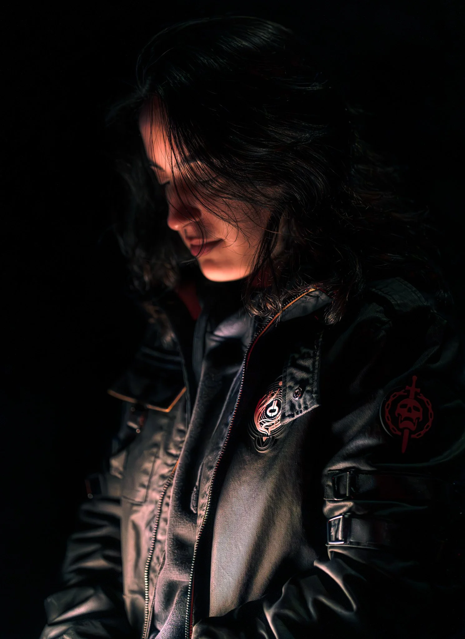 Person wearing a dark jacket with patches in dramatic lighting
