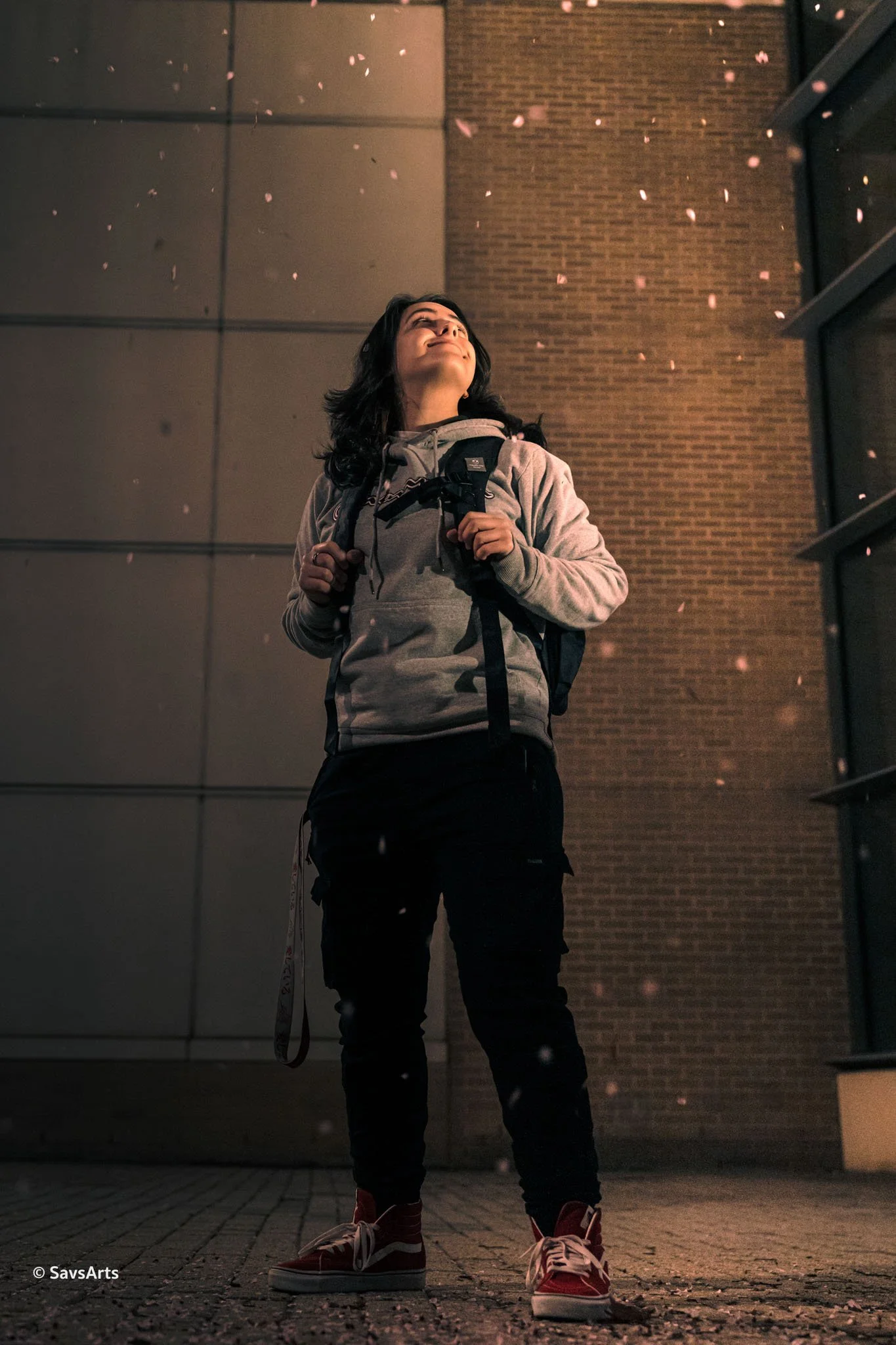 Person with a backpack looking up at night with falling petals