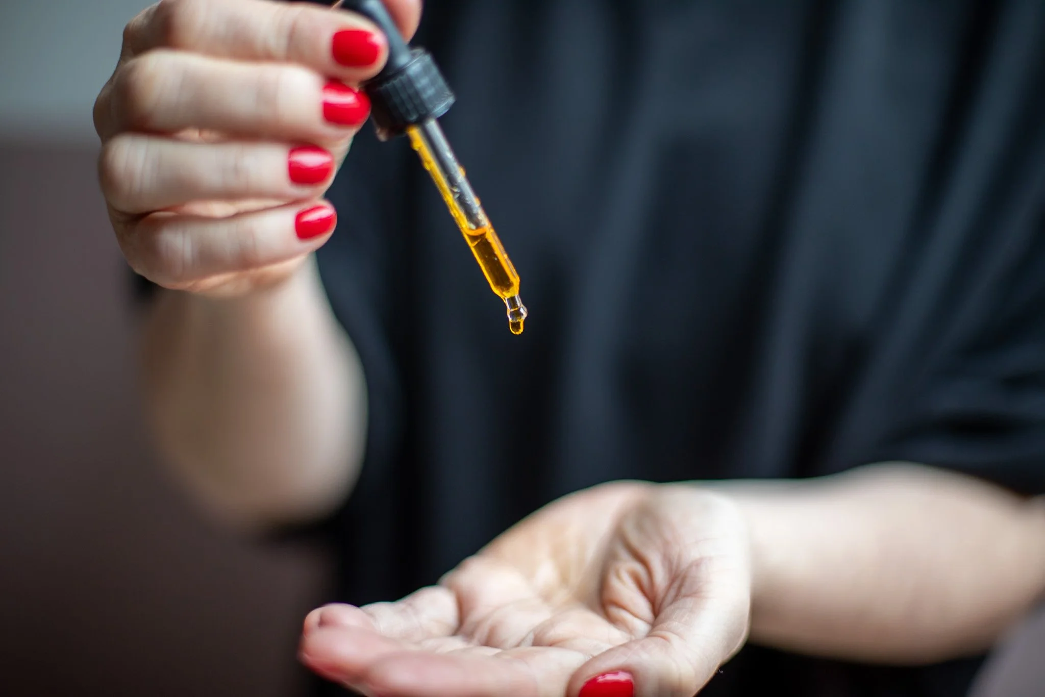 A white woman with red painted nails holding an essential oil dropper and massage oil is dropping into her hand