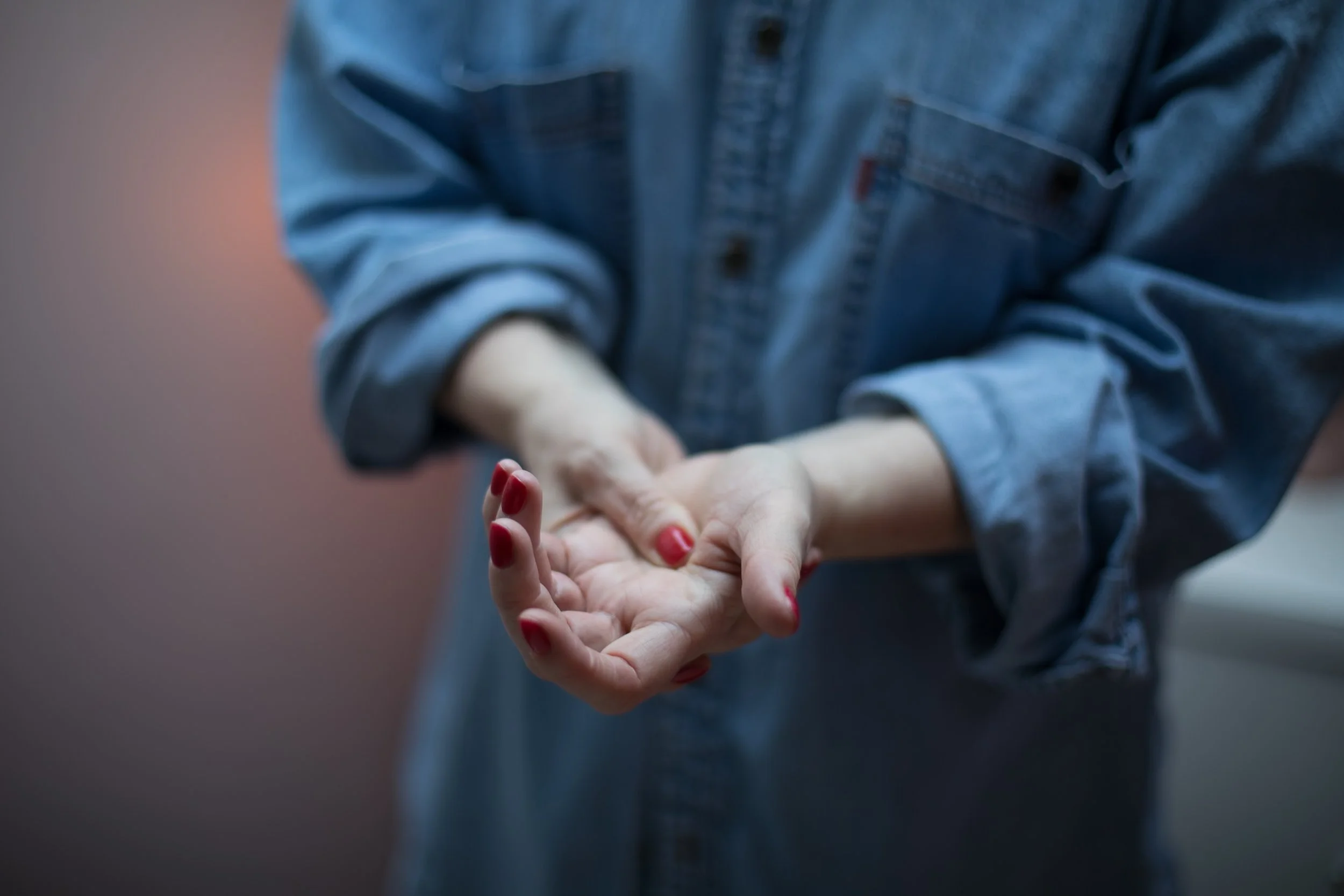 A white woman in a denim shirt with rolled up sleeves is using her thumb to activate acupressure points on her hand