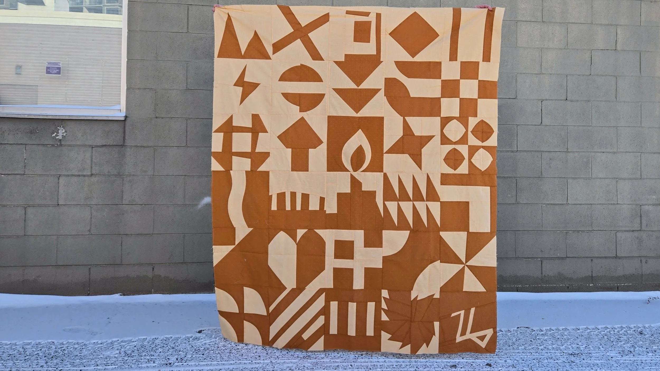 Warm brown and peachy yellow improvised quilt top in front of a concrete block wall