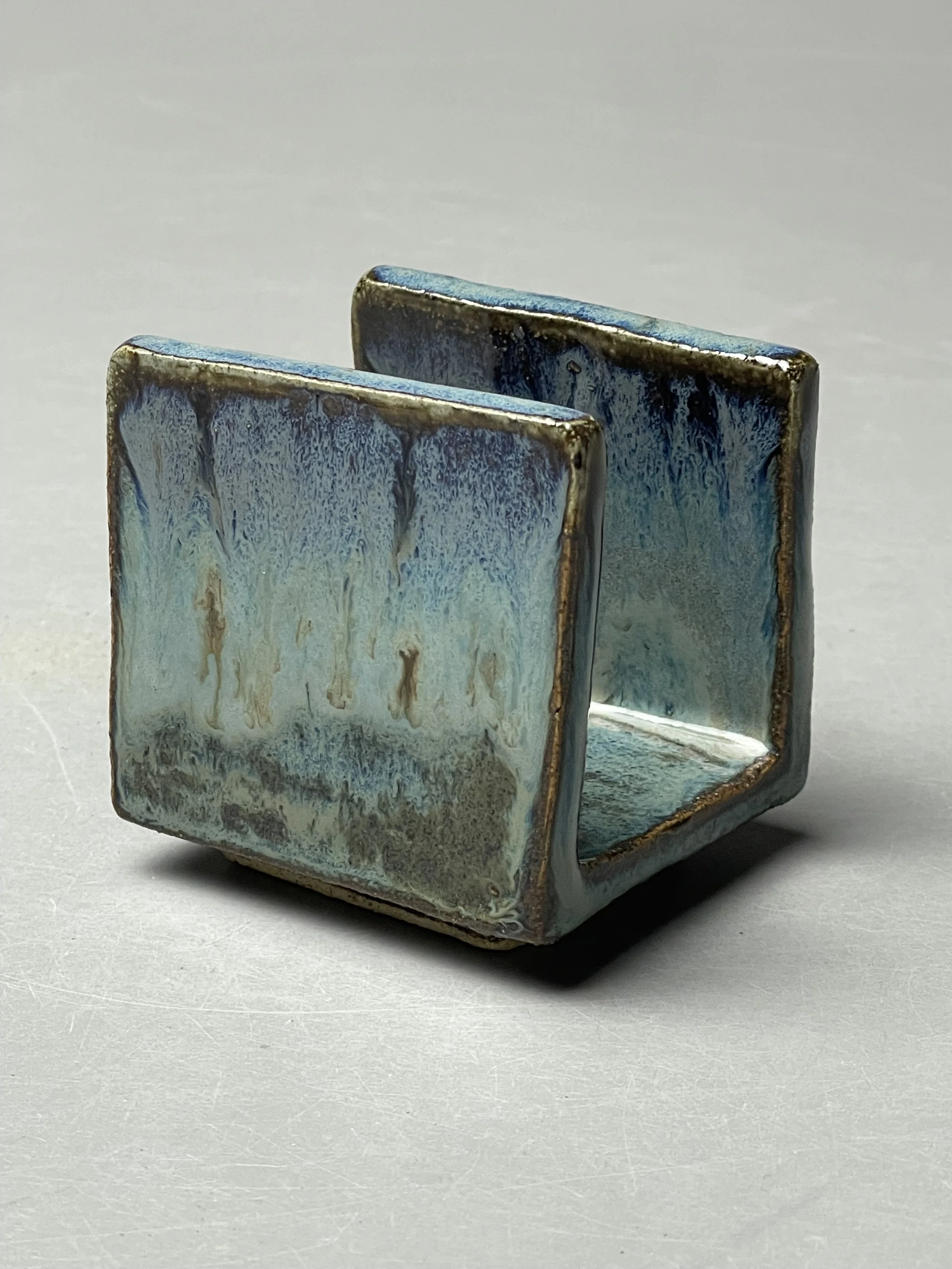 A sculpted ceramic tortoise with a rounded, white and brown shell and green head, resting on a beige fabric surface.