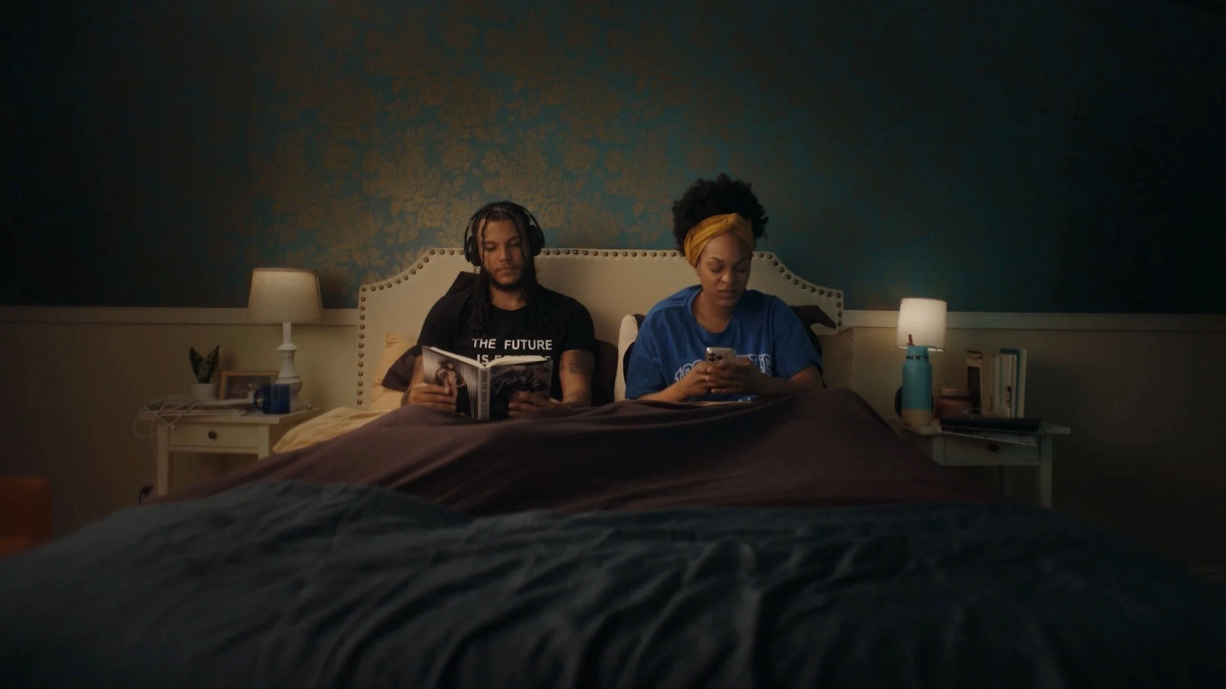 A couple sitting in bed with a book and smartphone.