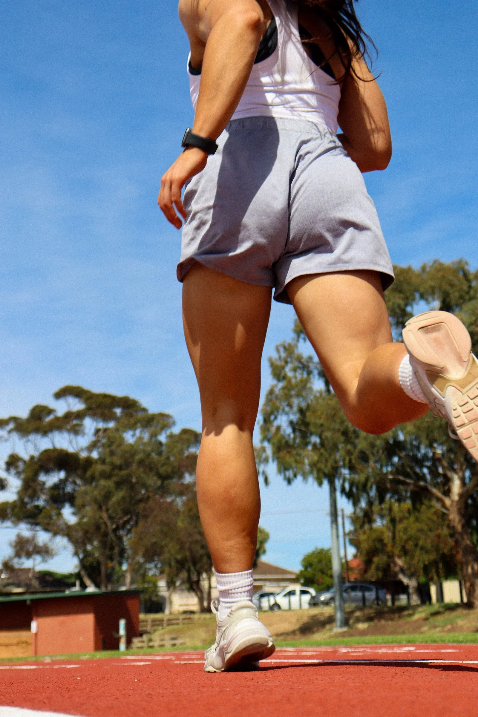 A person running on a track in an outdoor setting with trees and a blue sky.