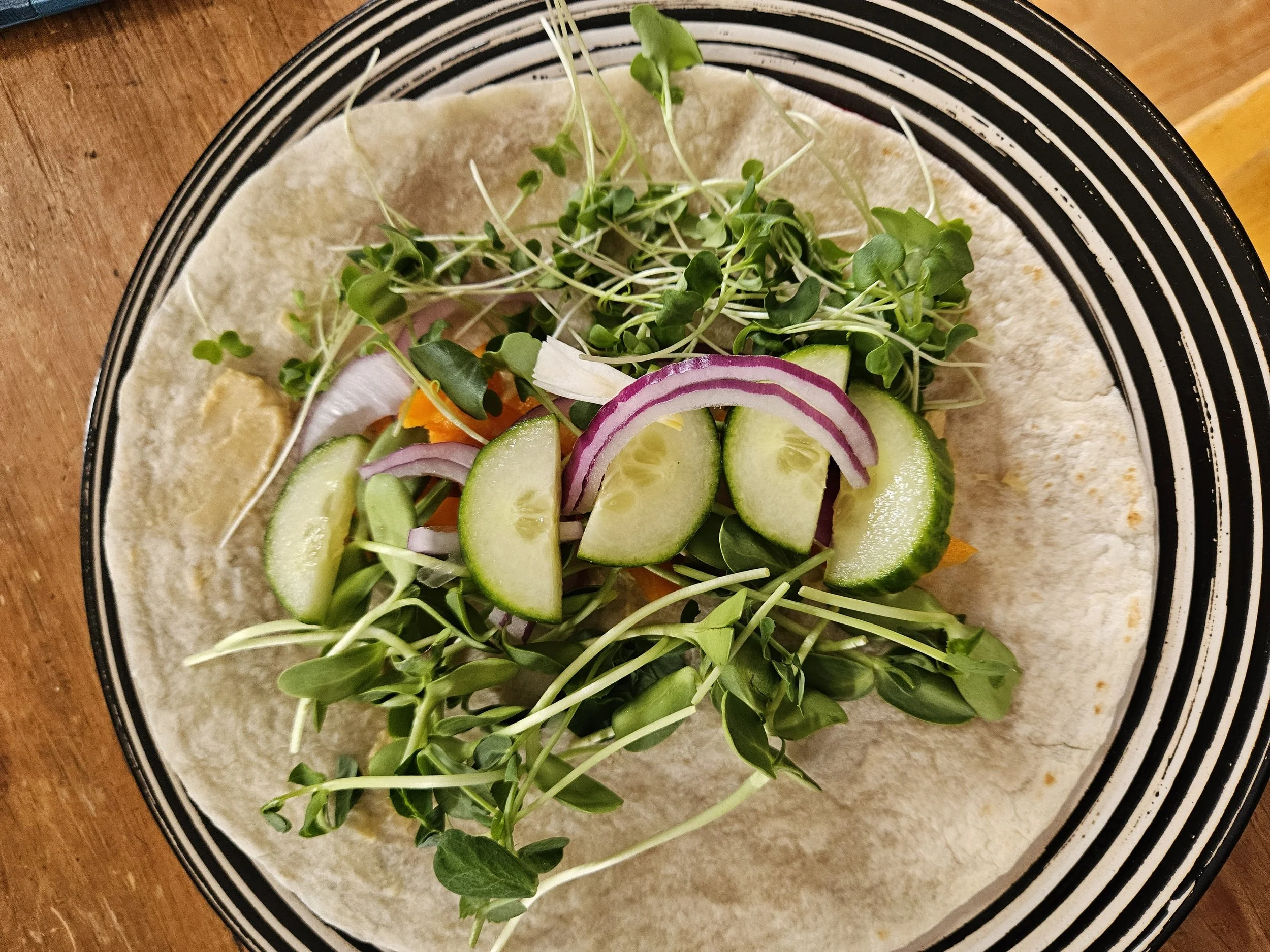Plate with a tortilla topped with microgreens, cucumber slices, and red onion.