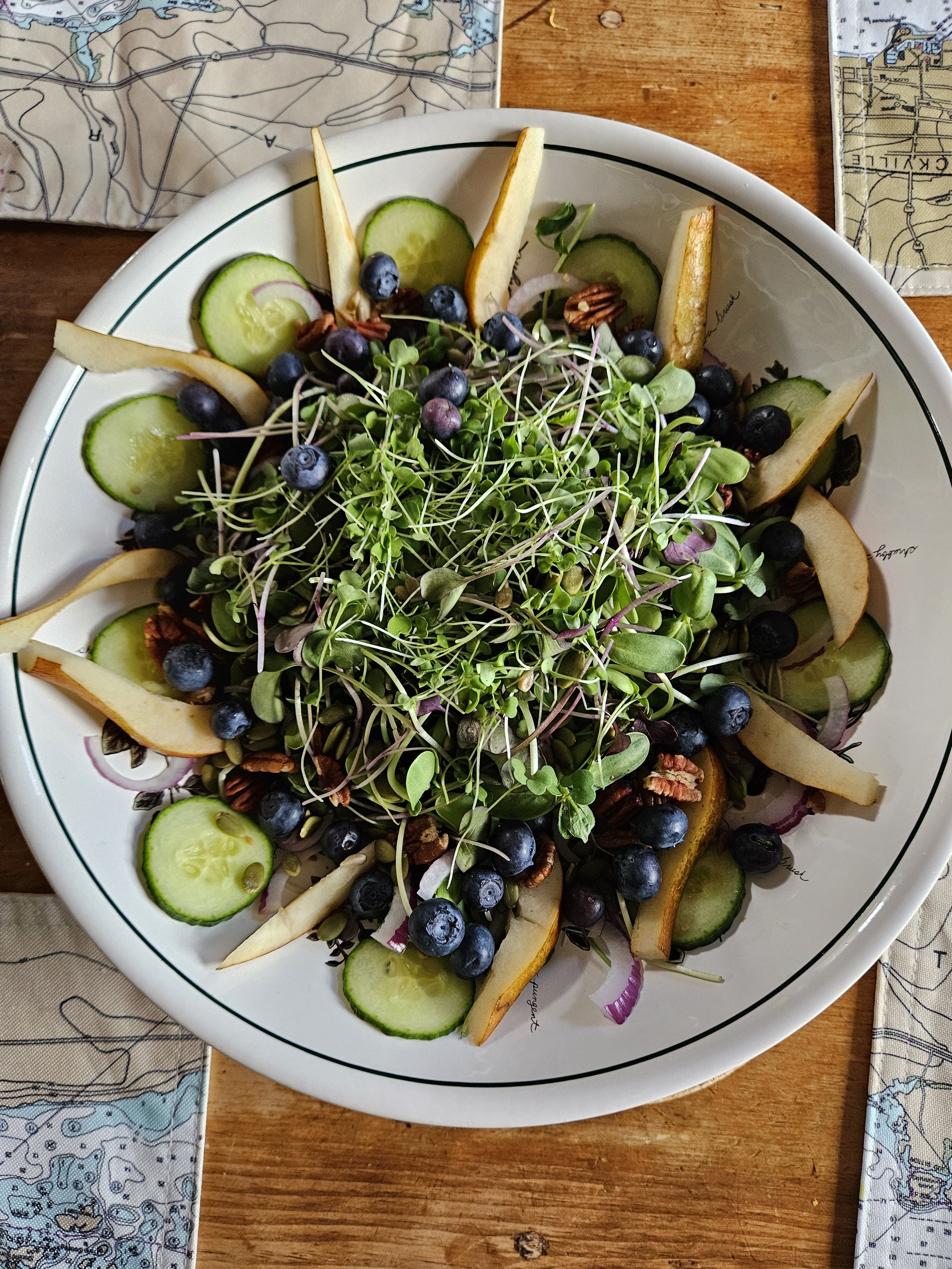 Salad with blueberries, cucumber slices, pear slices, microgreens, and pecans on a plate.