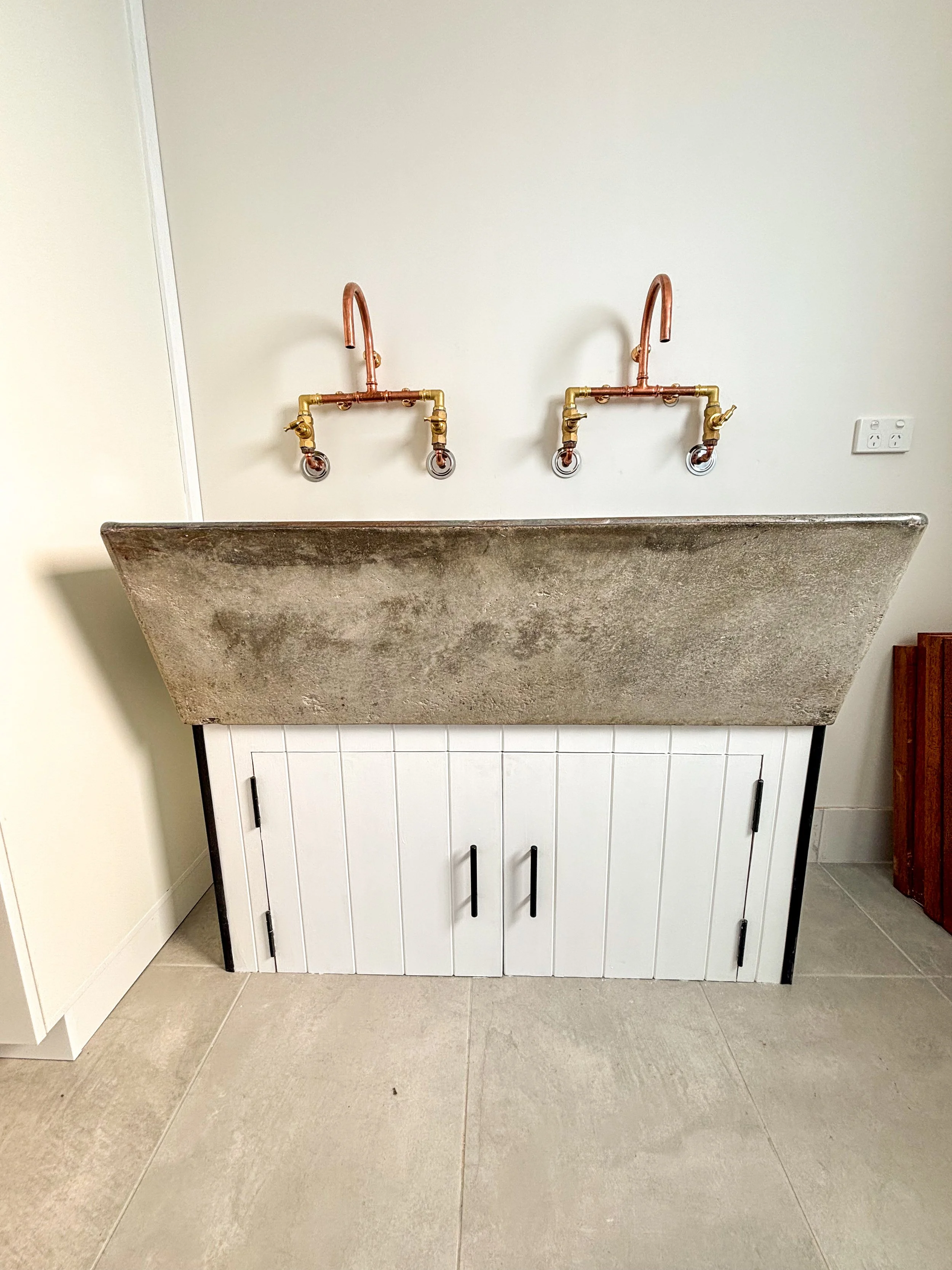 A simple and functional laundry room renovation with double utility sink,  stone basin and copper plumbing, mounted on white cabinet with black handles by Whitbuild, Cowra NSW