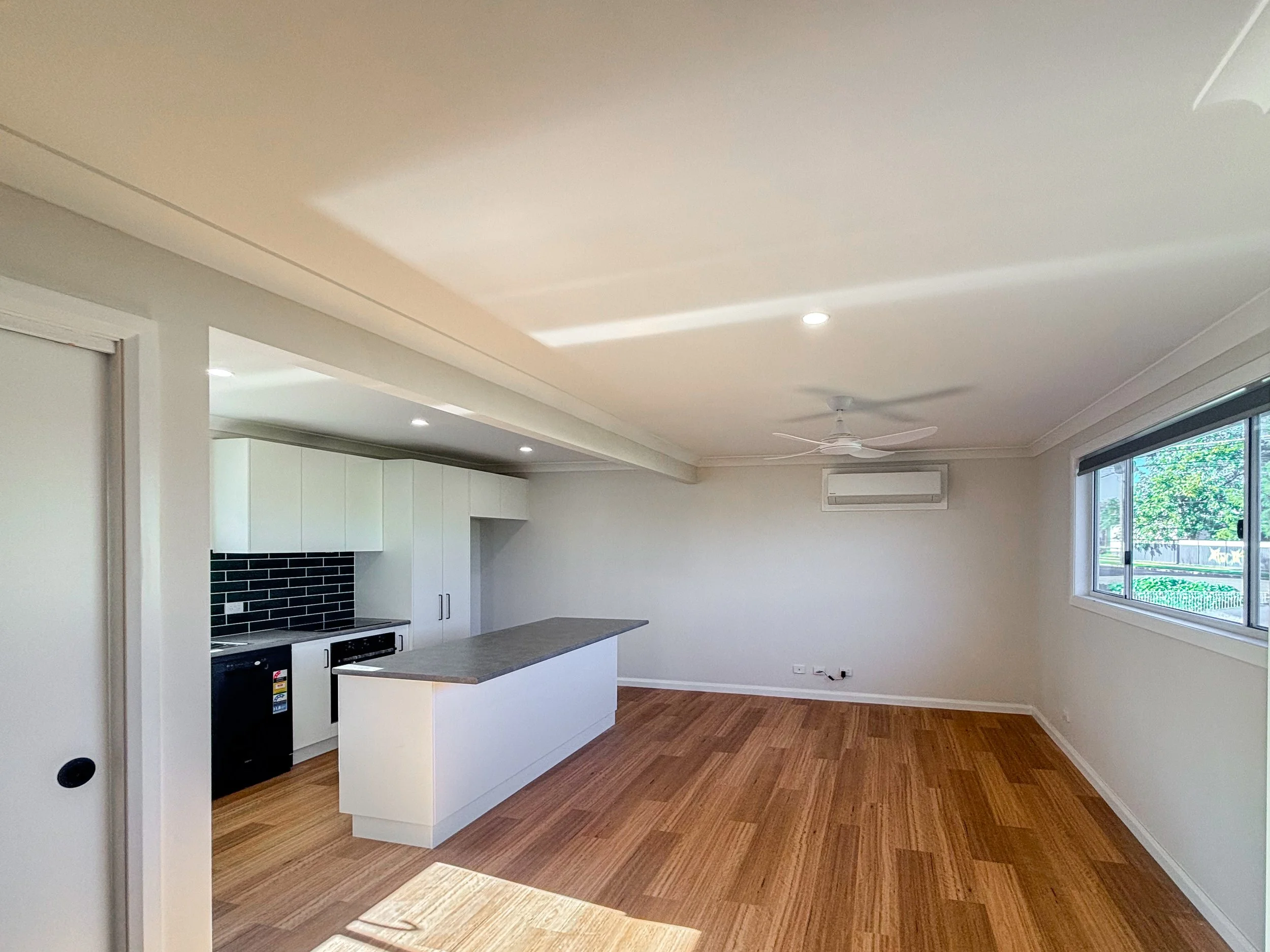 A modern, minimally decorated open-plan kitchen and living space renovation with large windows letting in natural light by Whitbuild, Cowra NSW