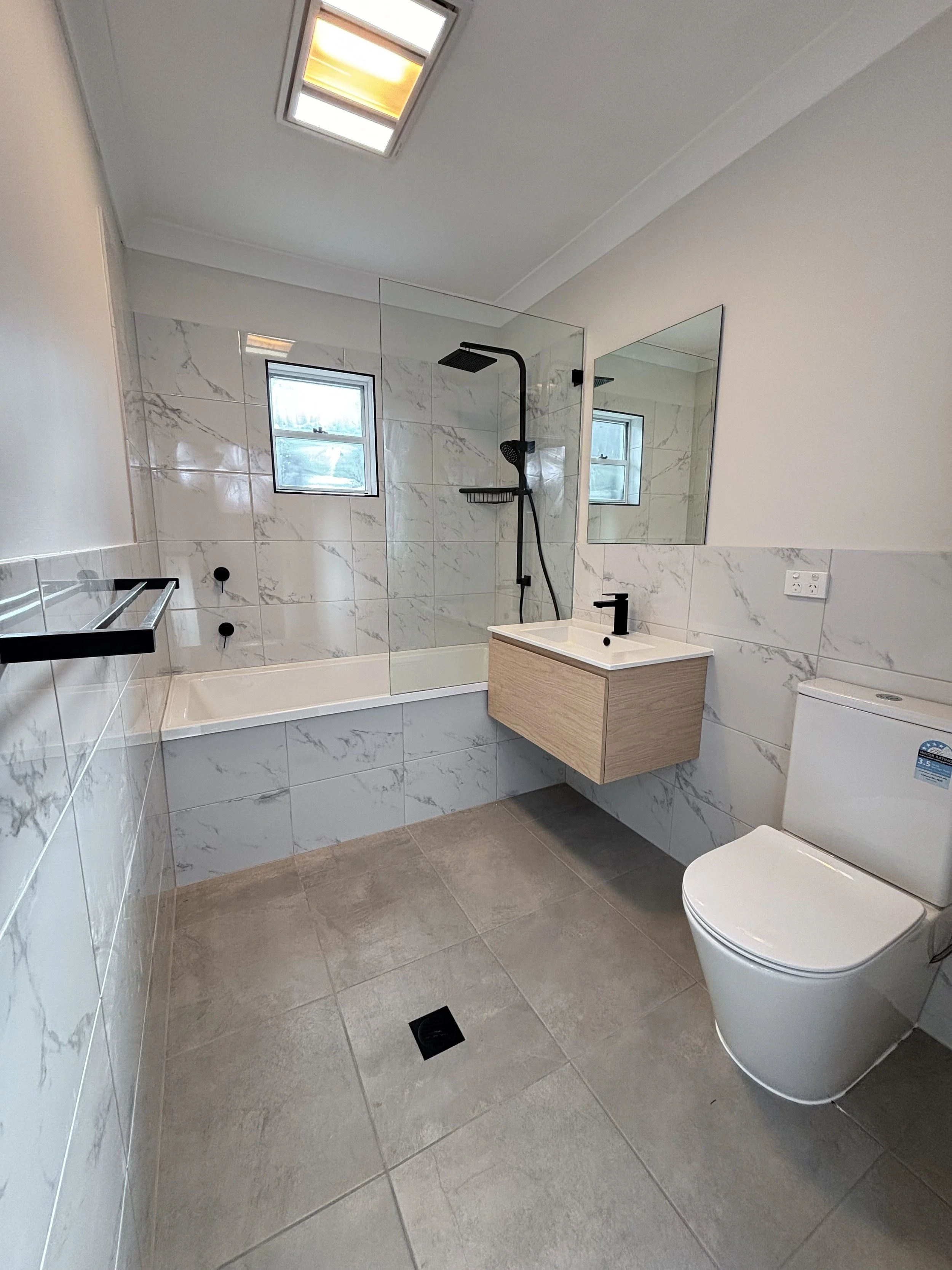 A modern bathroom renovation with walls are decorated with white marble tiles and practical design by Whitbuild, Cowra, NSW