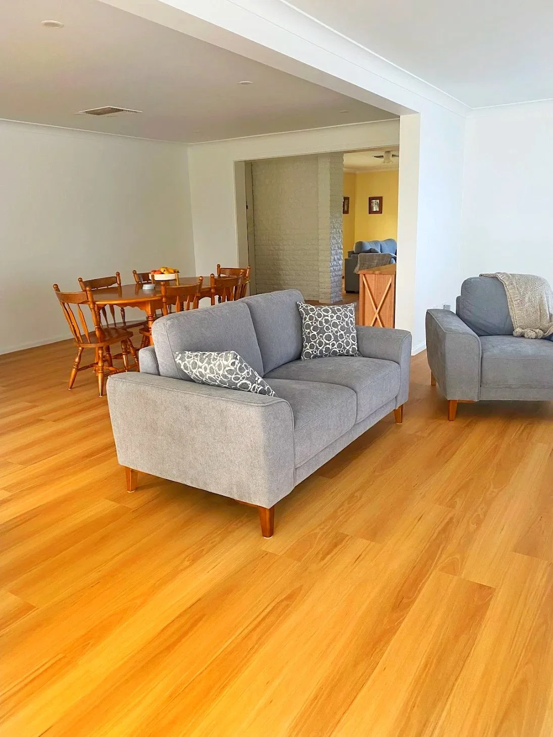 Living room with two gray sofas, wooden flooring, and a doorway leading to a dining area with a round wooden table and matching chairs.