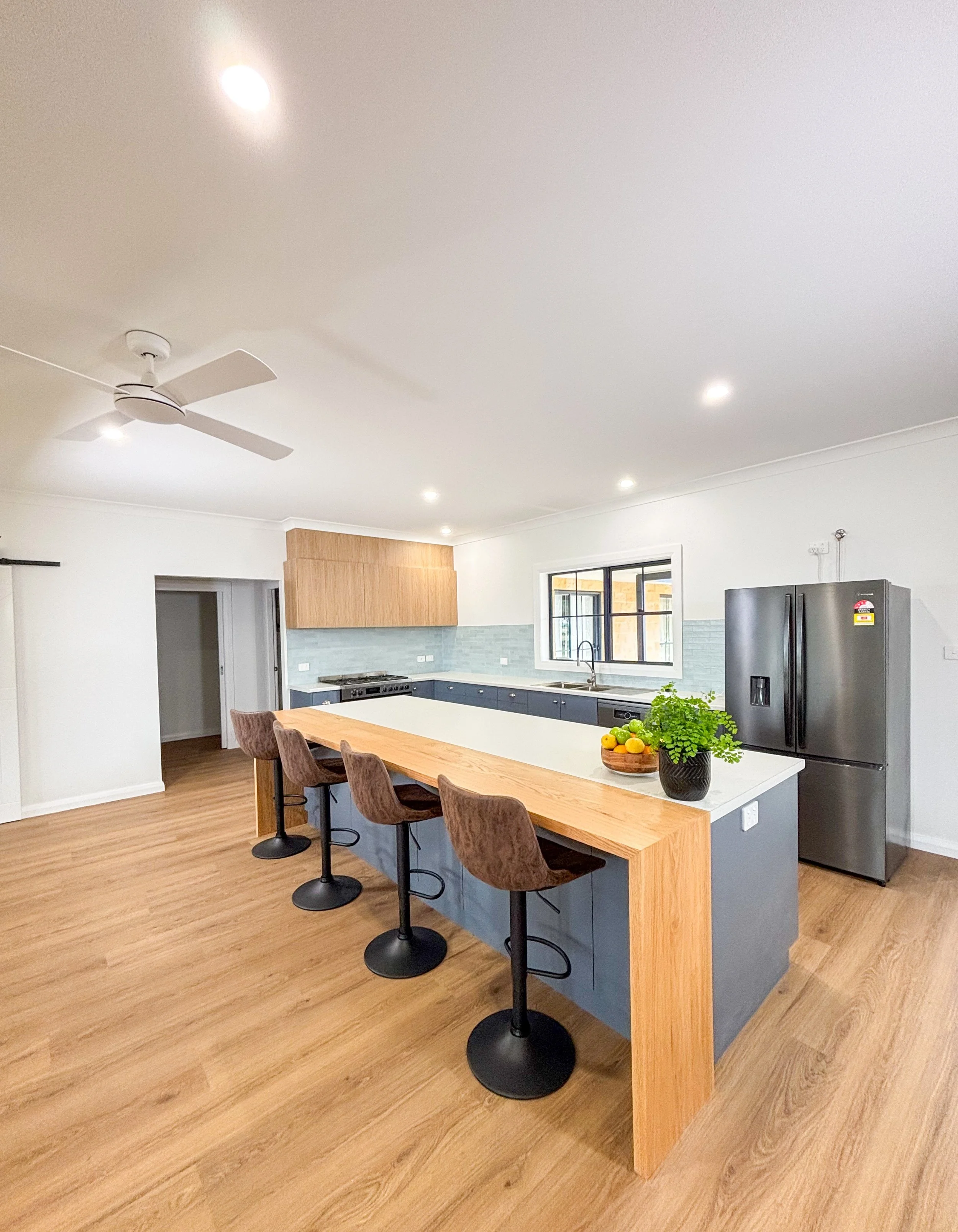 A modern kitchen renovation with a large island, dark blue cabinets, a window, and a wooden dining table by Whitbuild, Forbes NSW