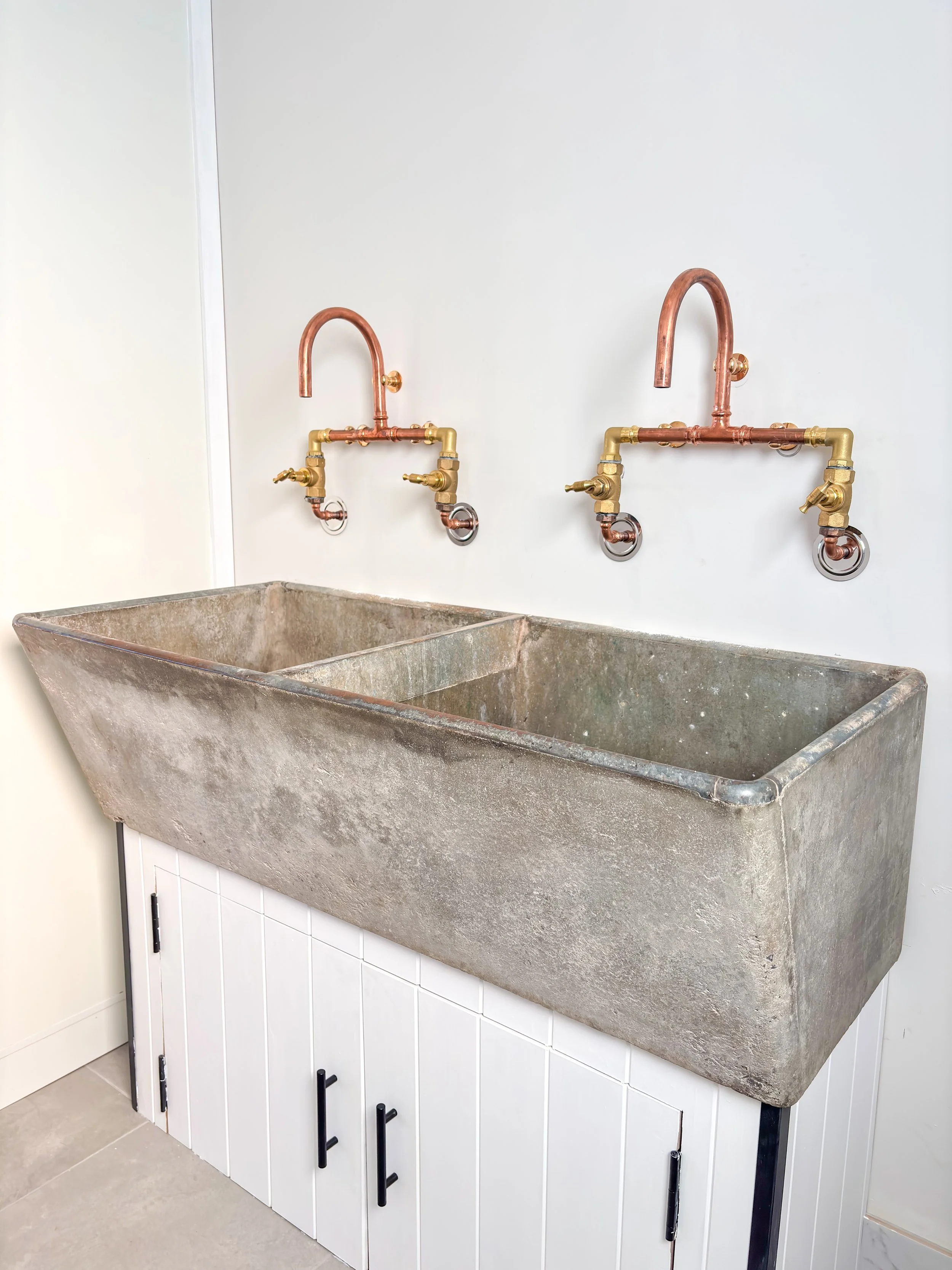 A simple and functional laundry room renovation with double utility sink,  stone basin and copper plumbing, mounted on white cabinet with black handles by Whitbuild, Cowra NSW
