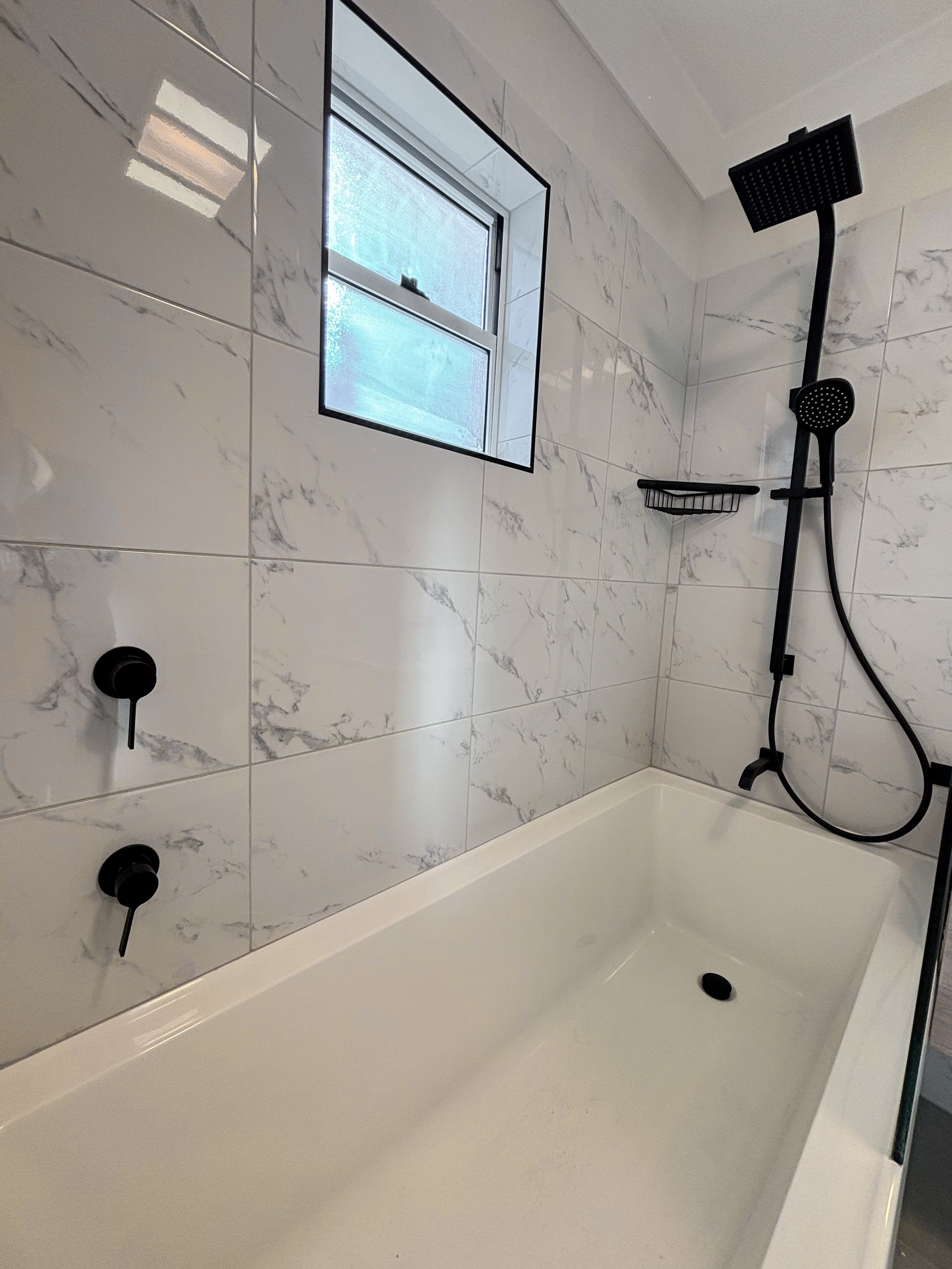 A modern bathroom renovation with walls are decorated with white marble tiles and practical design by Whitbuild, Cowra, NSW