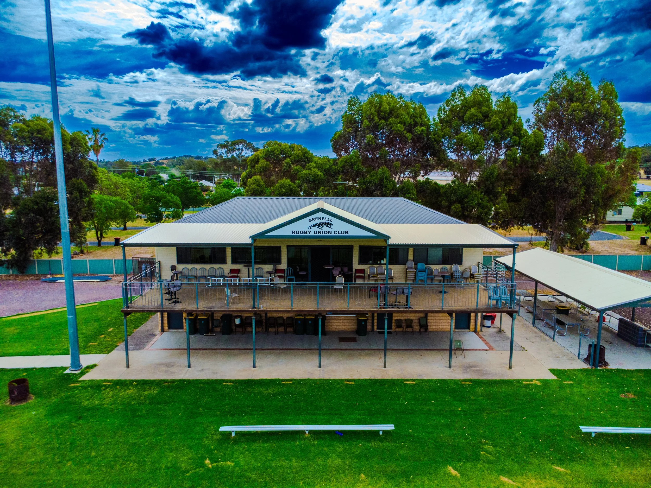 Outdoor view of the Grenfell Rugby Union Club building with a gray roof, surrounded by green trees and a grassy area, under a partly cloudy sky.