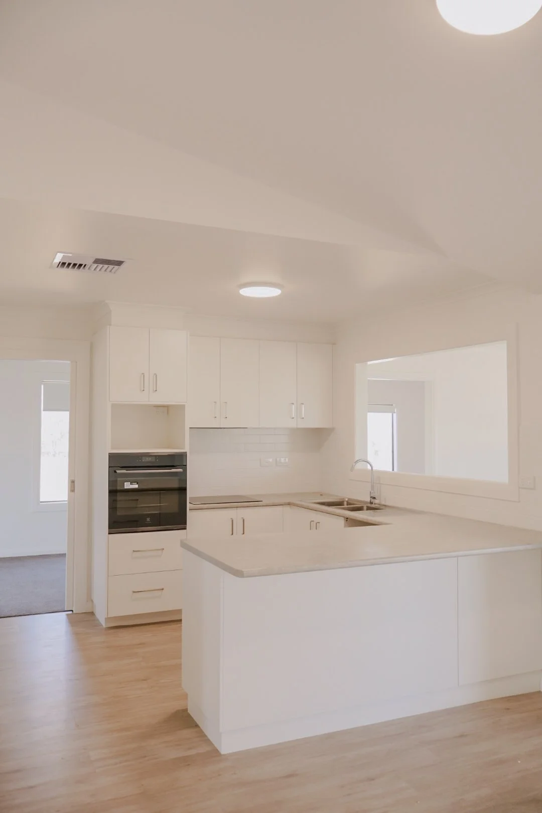 Modern kitchen with white cabinets, a gray kitchen island with wooden bar stools, white countertops, a brick tile backsplash, and appliances including a microwave, oven, refrigerator, and a coffee maker.