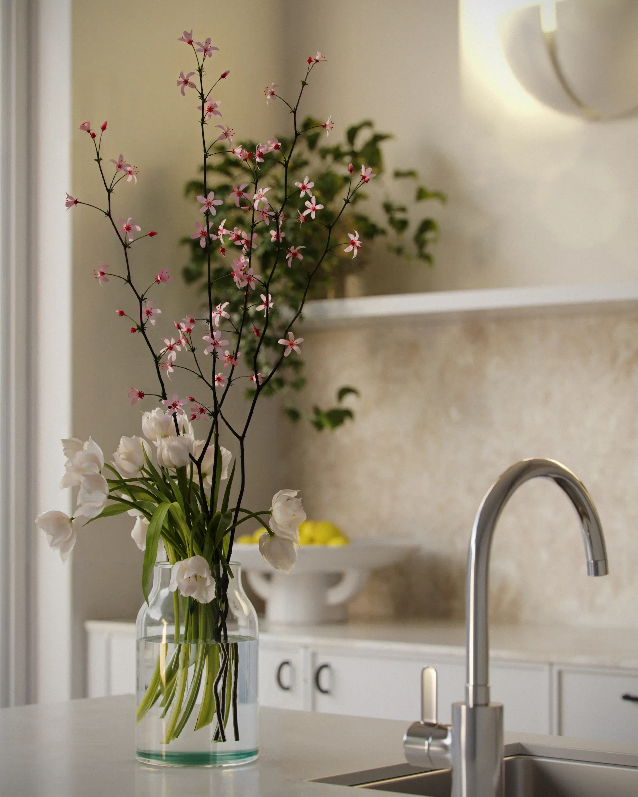 A vase with white and pink flowers on a kitchen countertop, with a faucet and a bowl of yellow lemons in the background.