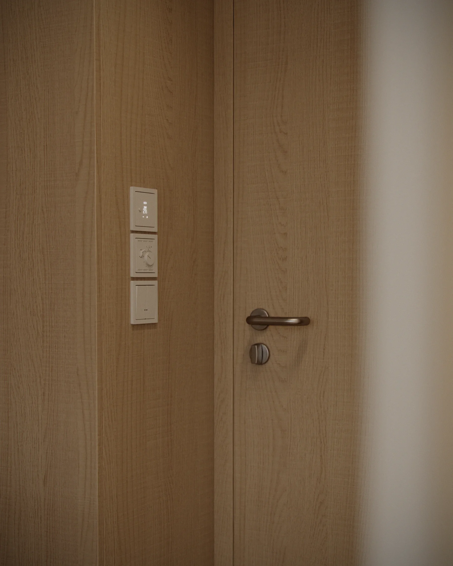 A wooden door with a silver handle, and three white control panels on the wall next to it.