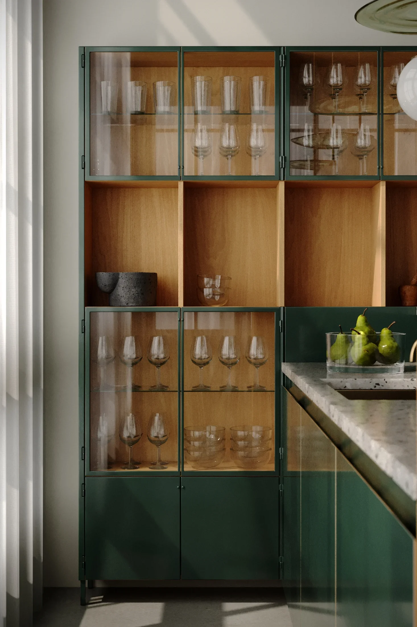 A green and wooden cabinet with glass doors containing glassware and bowls, next to a countertop with pears.