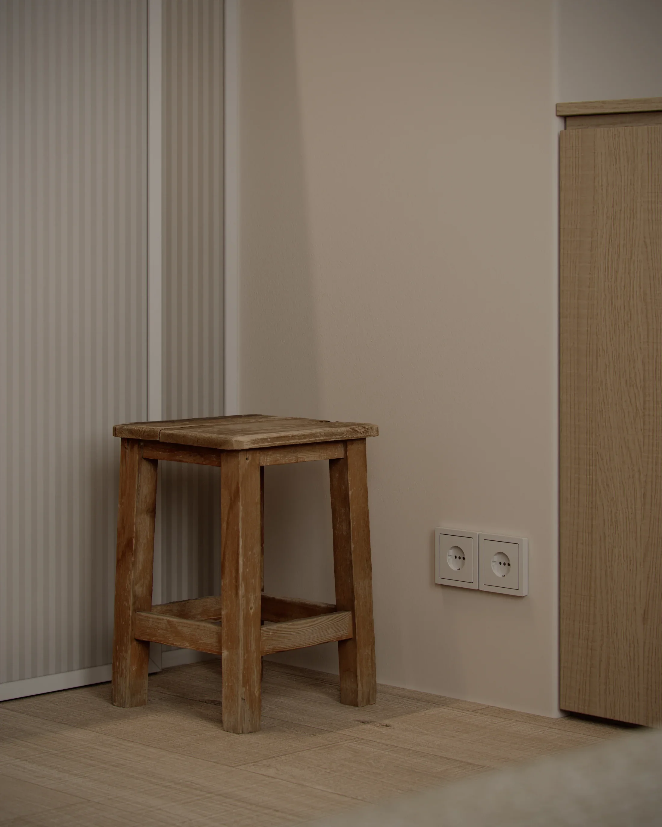 A small rustic wooden stool in a corner of a room near electrical outlets and a wooden cabinet.