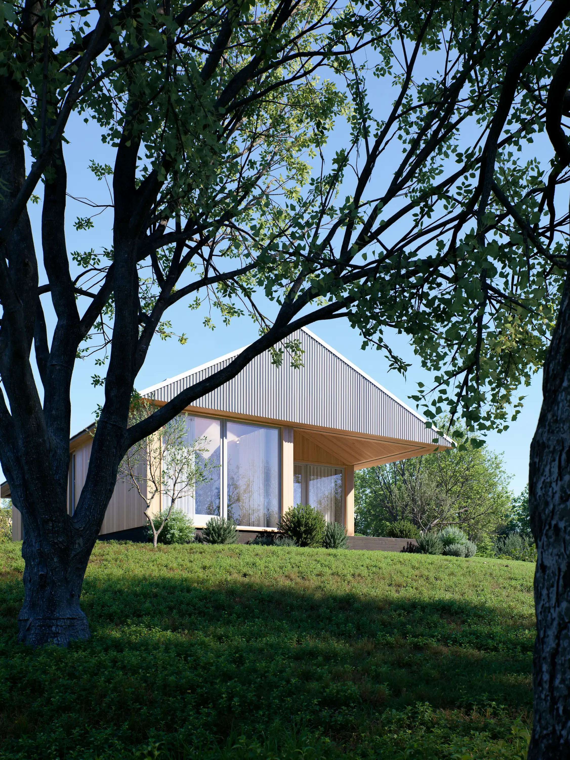 Modern house with large windows on a grassy hill, framed by trees, under a clear blue sky.