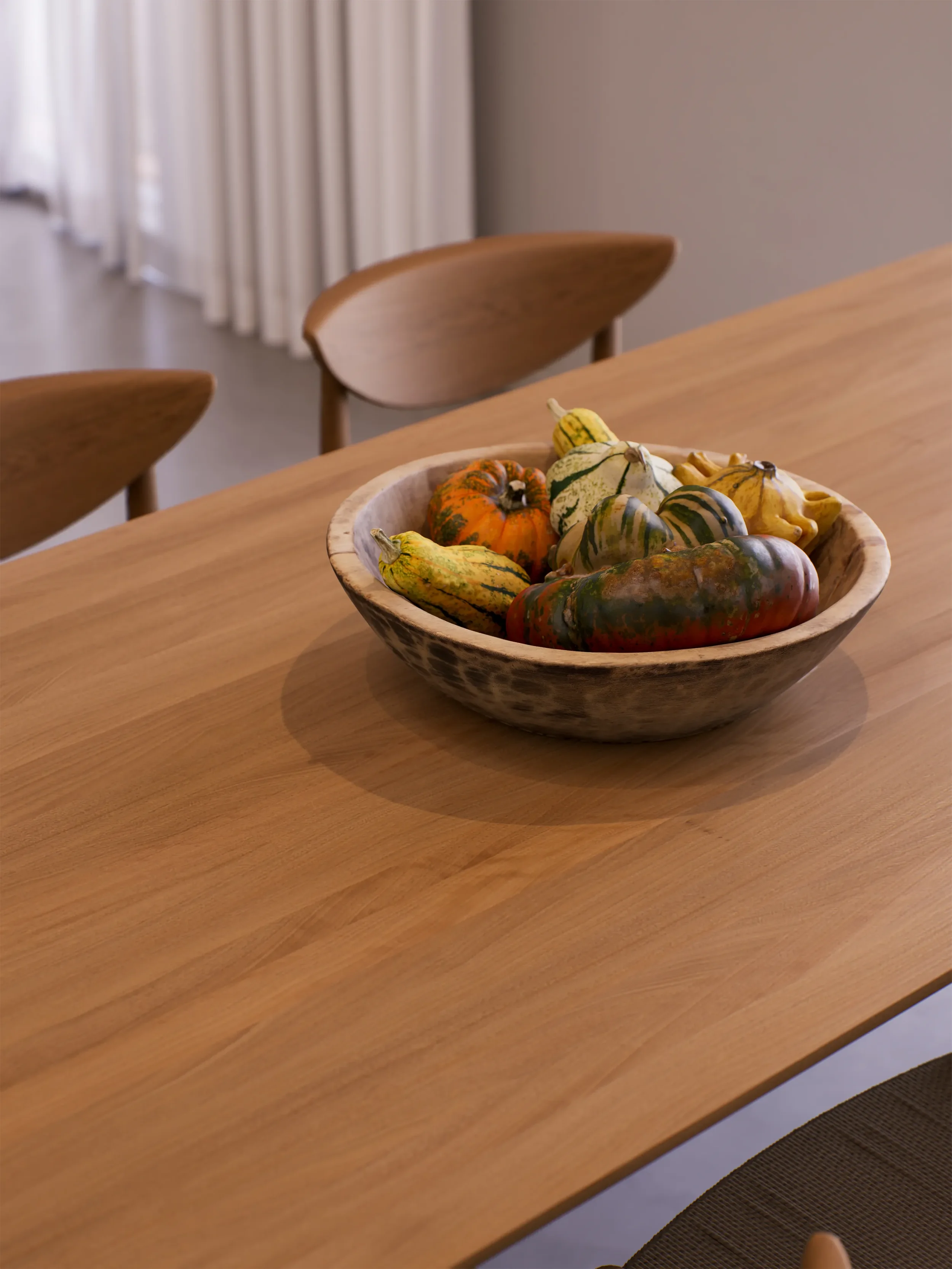 A wooden dining table with a ceramic bowl filled with various colorful gourds and small pumpkins, positioned near a window with curtains.