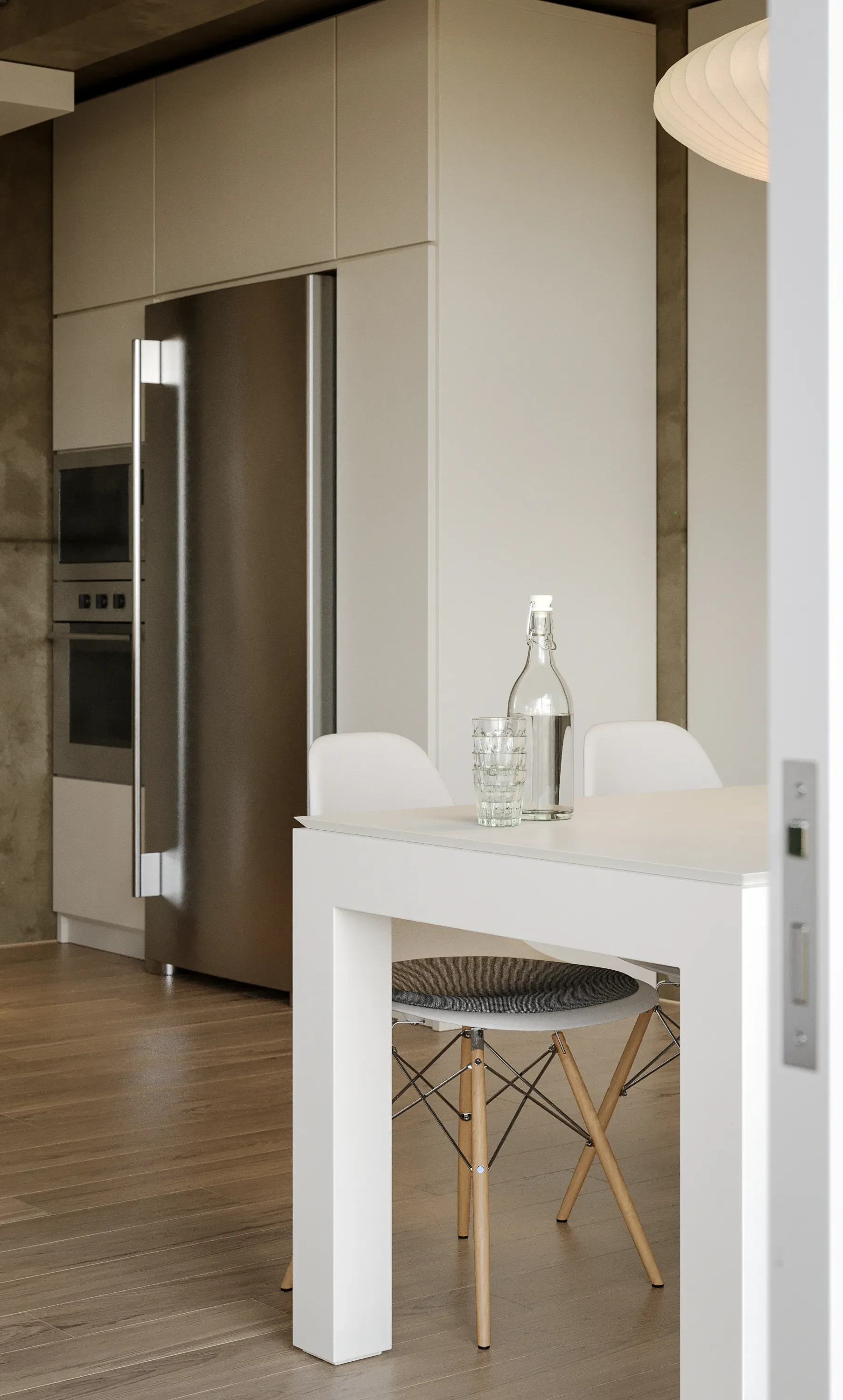 Modern kitchen and dining area with a white table, two white chairs, a glass water bottle, and a glass of water, with a stainless steel refrigerator and built-in oven in the background.
