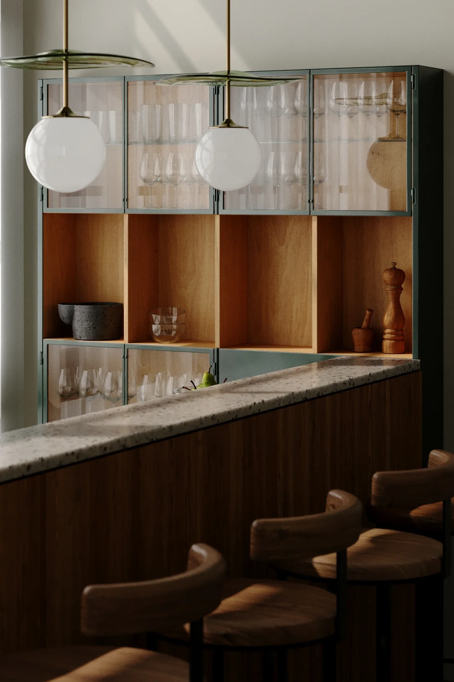 A kitchen with a wooden cabinet with glass doors on top, showcasing wine glasses and a few pieces of pottery inside. Below the cabinet, there are open cubbies, some with additional glasses and a pear. A granite countertop runs along the foreground, w