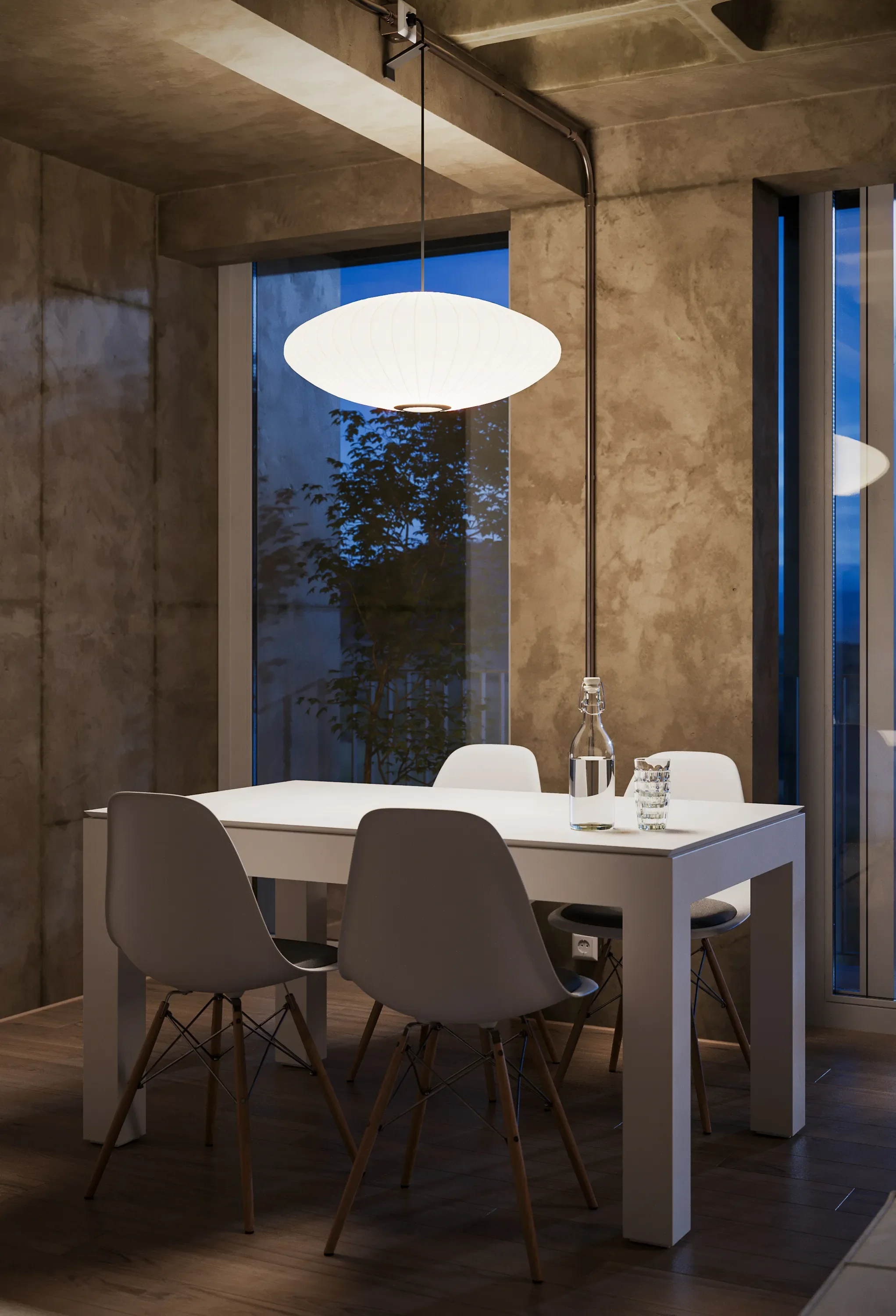 A modern dining room with a white table, three white chairs, a hanging paper lantern, a glass water bottle and a glass of water on the table, and large windows showing the evening sky and trees outside.