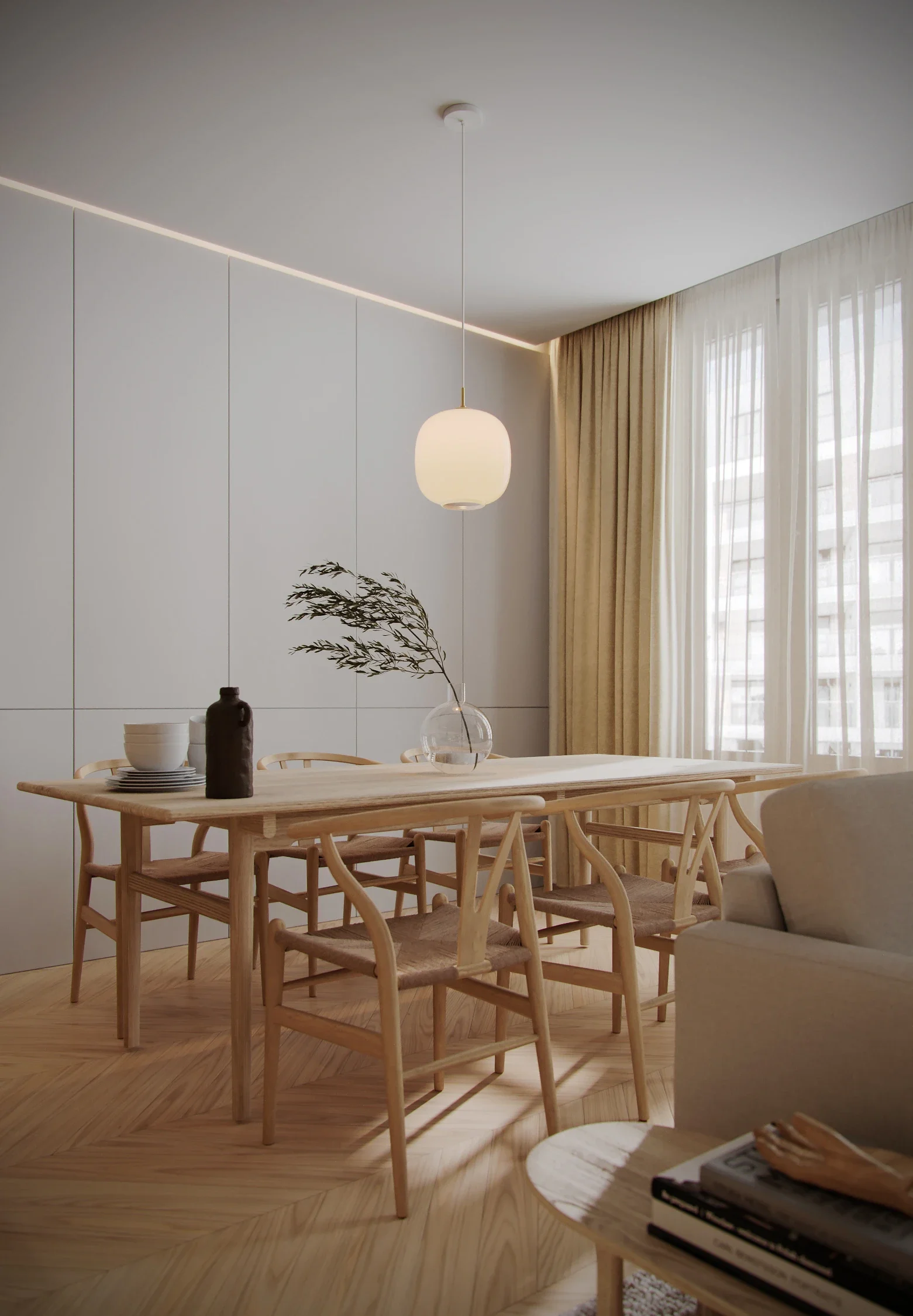 Minimalist dining room with light wood table, six matching chairs, a beige sofa, a small round side table with magazines, a glass vase with a single branch, ceramic bowls, and a black bottle. Bright natural light from large windows with sheer curtain
