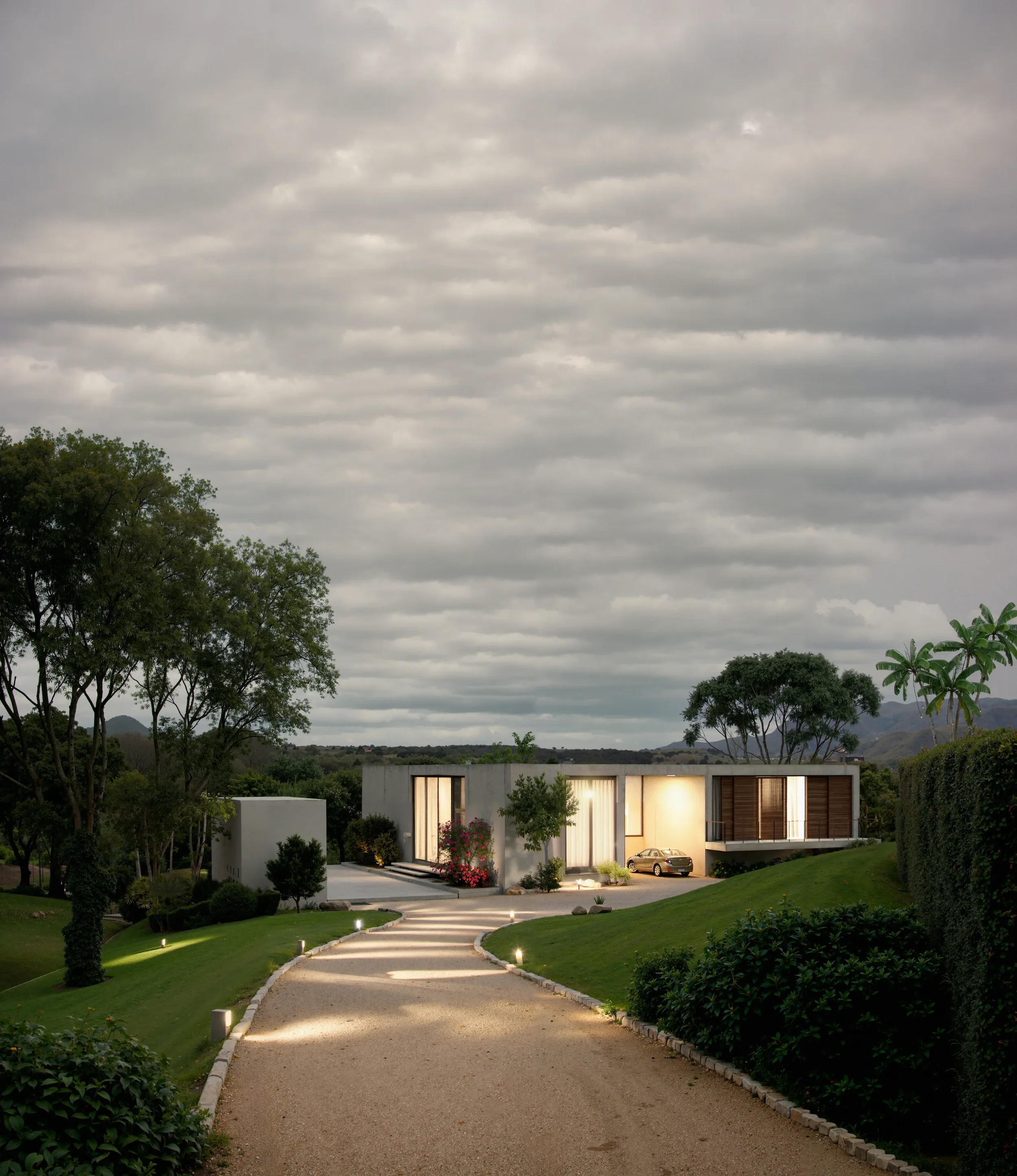 Modern single-story house with large windows, surrounded by greenery, with a curved gravel driveway and outdoor lighting.