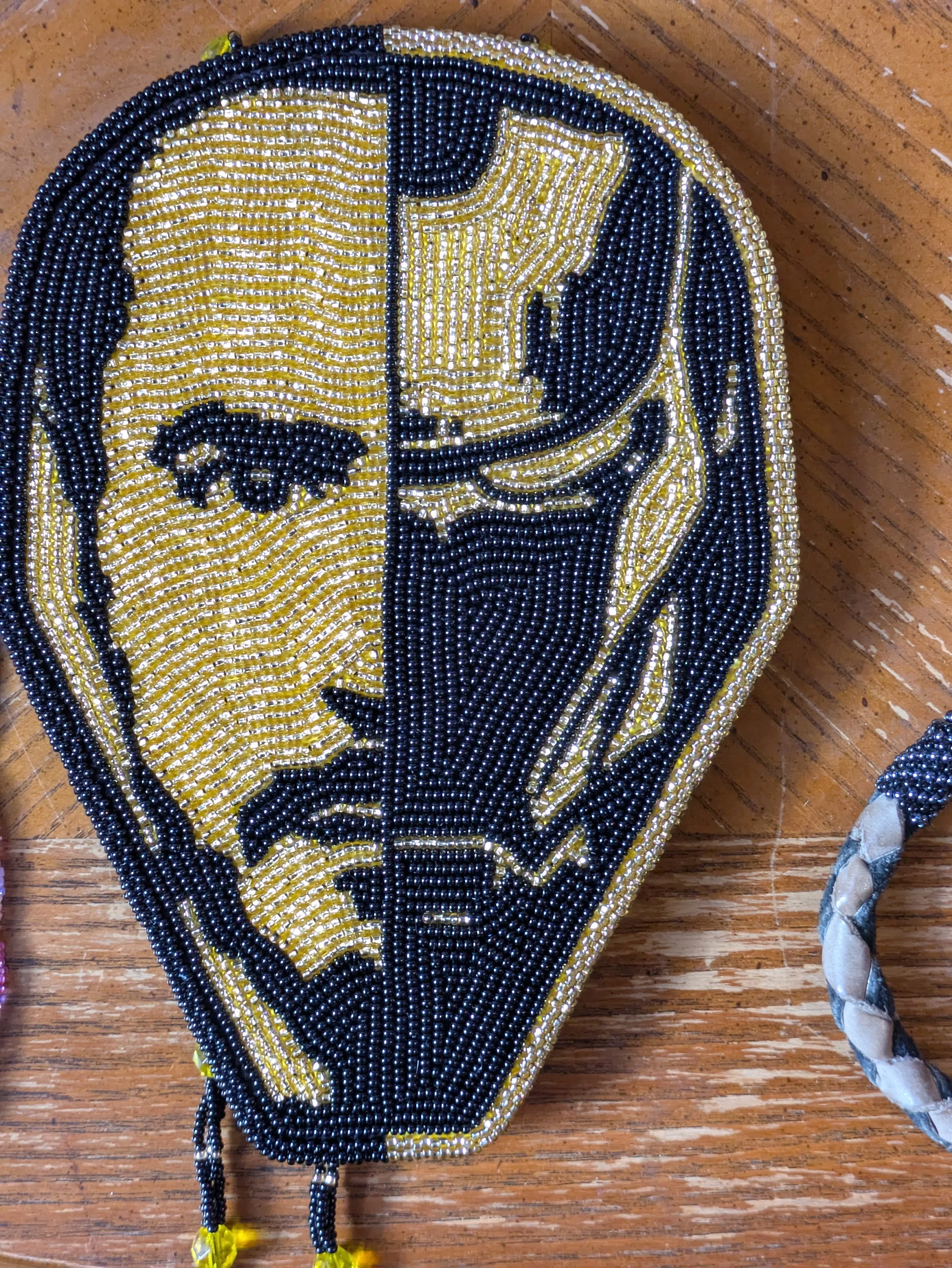 Beadwork of a face that is half Iron Man and half Tony Stark, in black and gold