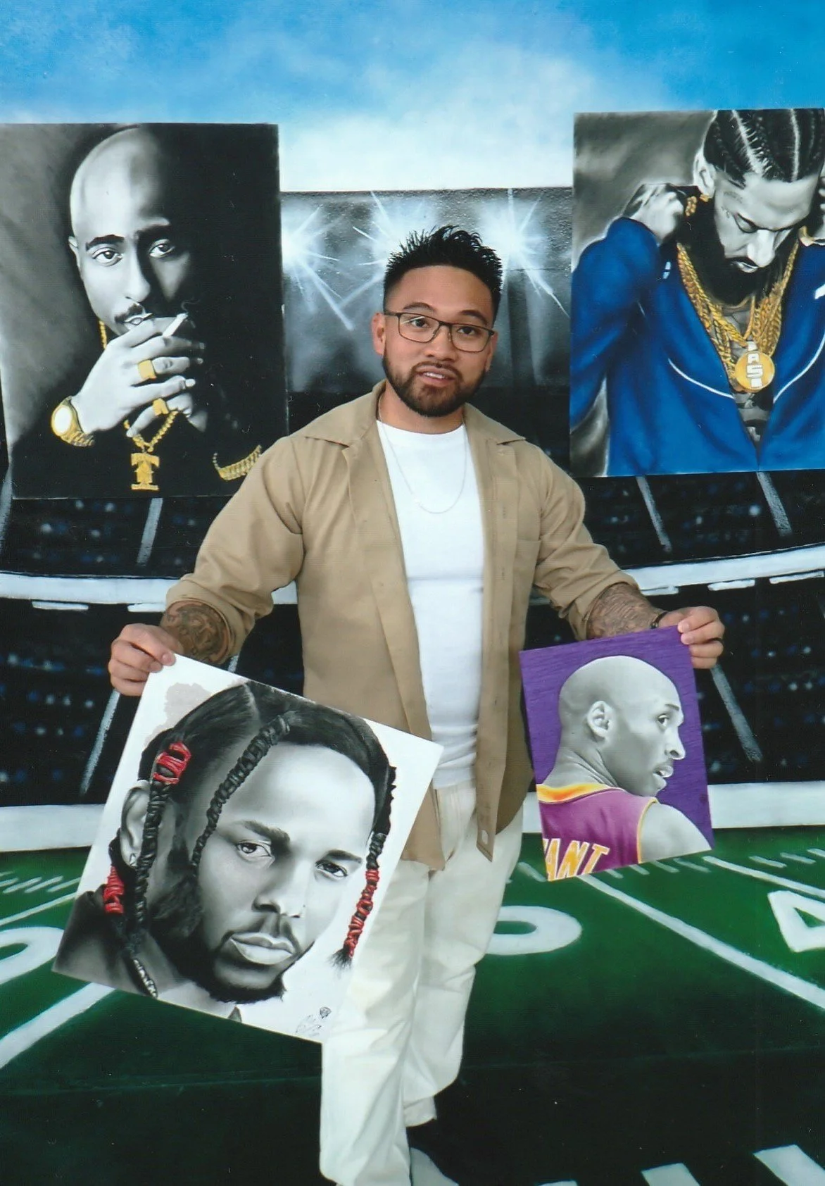 Photo of a man holding pieces of artwork with a background of a stadium