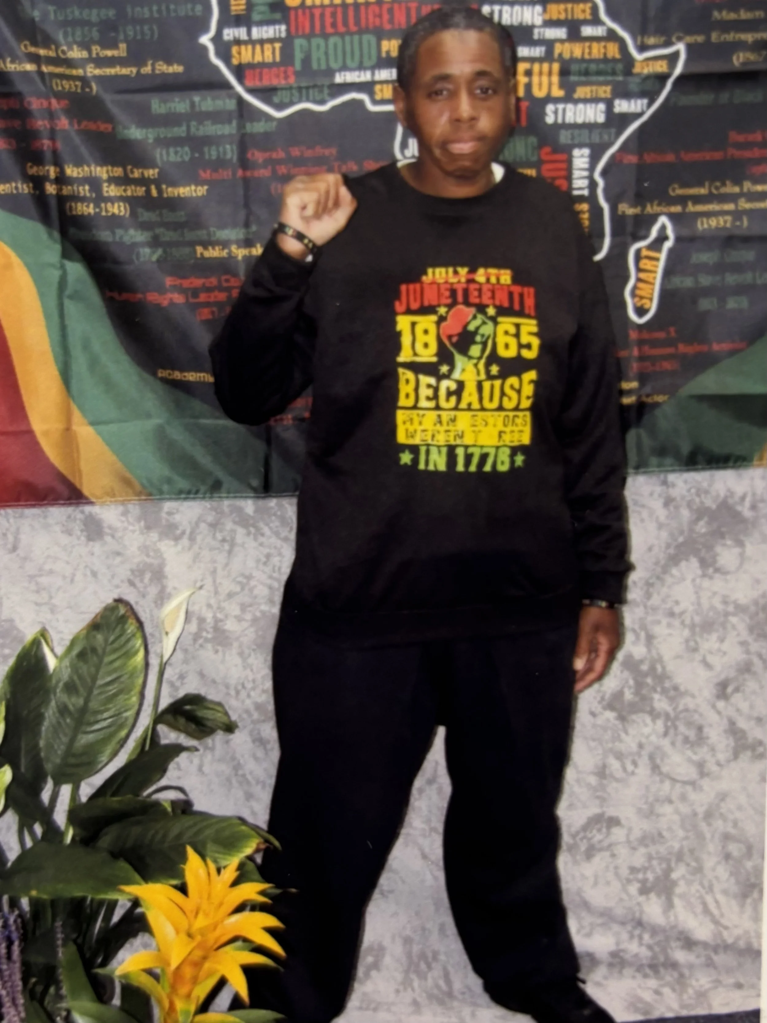 Photo of a person holding up a Black Power fist and wearing a Juneteenth sweatshirt