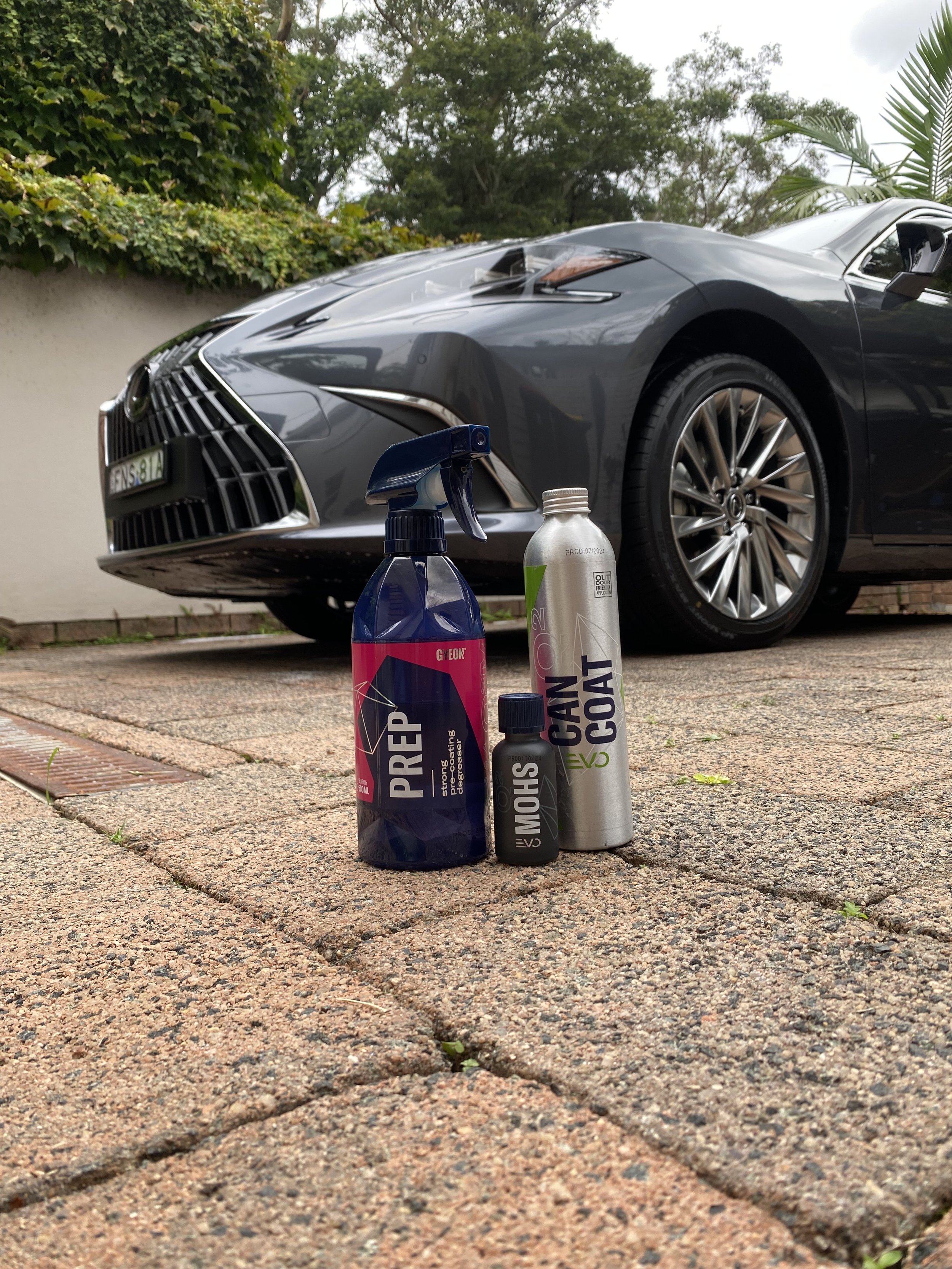 Car detailing products in front of a gray car on a driveway