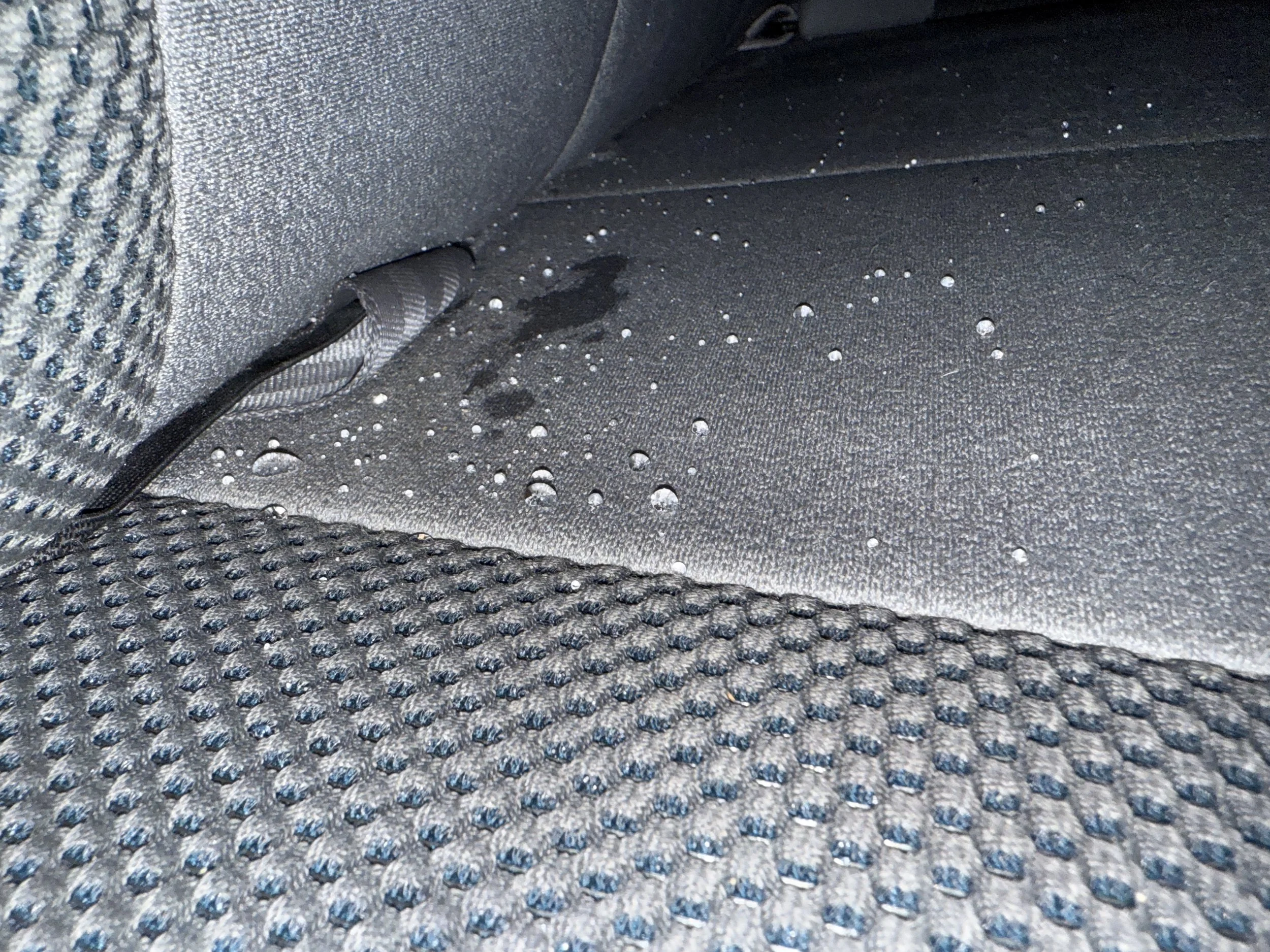 Car interior with water droplets on the black fabric seat and floor mat.