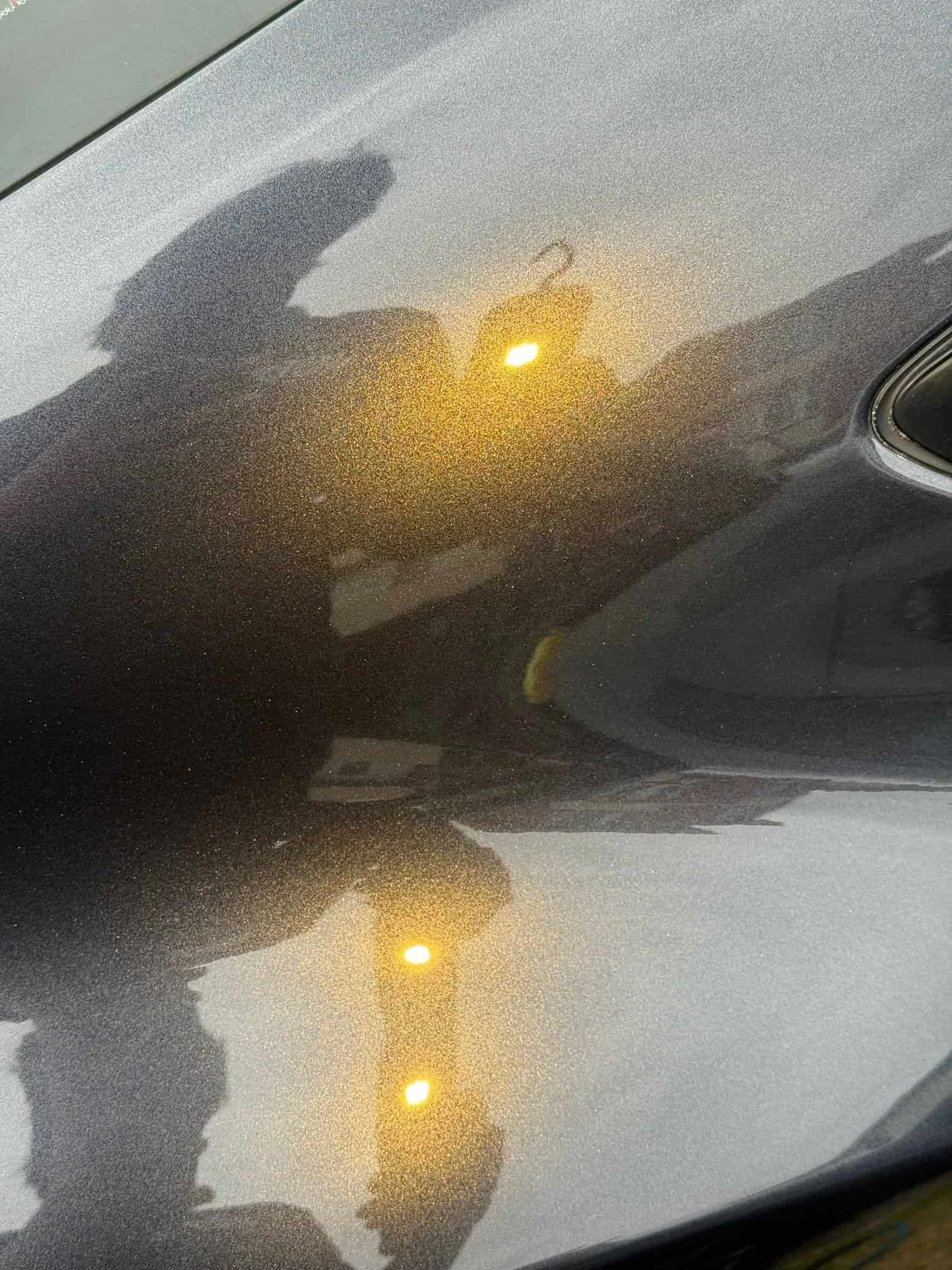 Close-up of a car’s shiny gray surface with ceramic coating Wollongong, reflecting two yellow lights and a person’s silhouette.