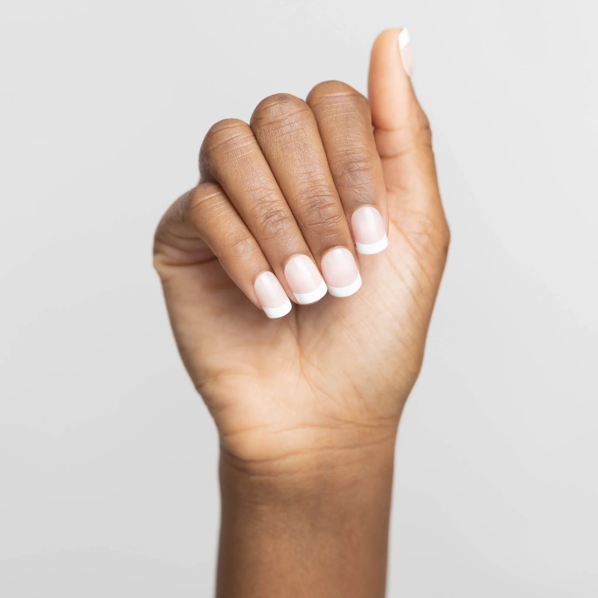 Close-up of a hand with a French manicure against a light background.