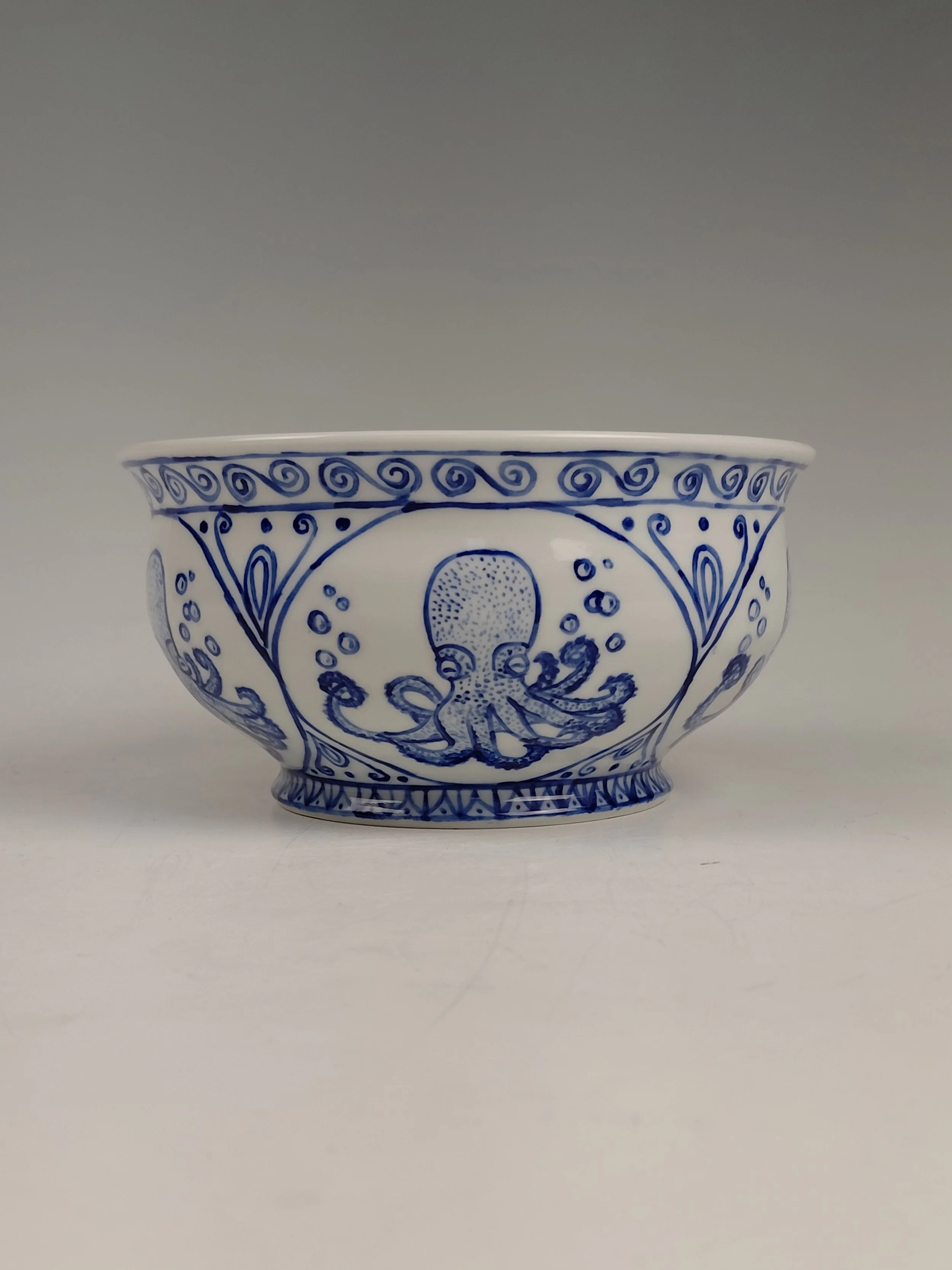 White ceramic bowl with blue decorative pattern featuring an octopus and intricate designs, set against a plain background.