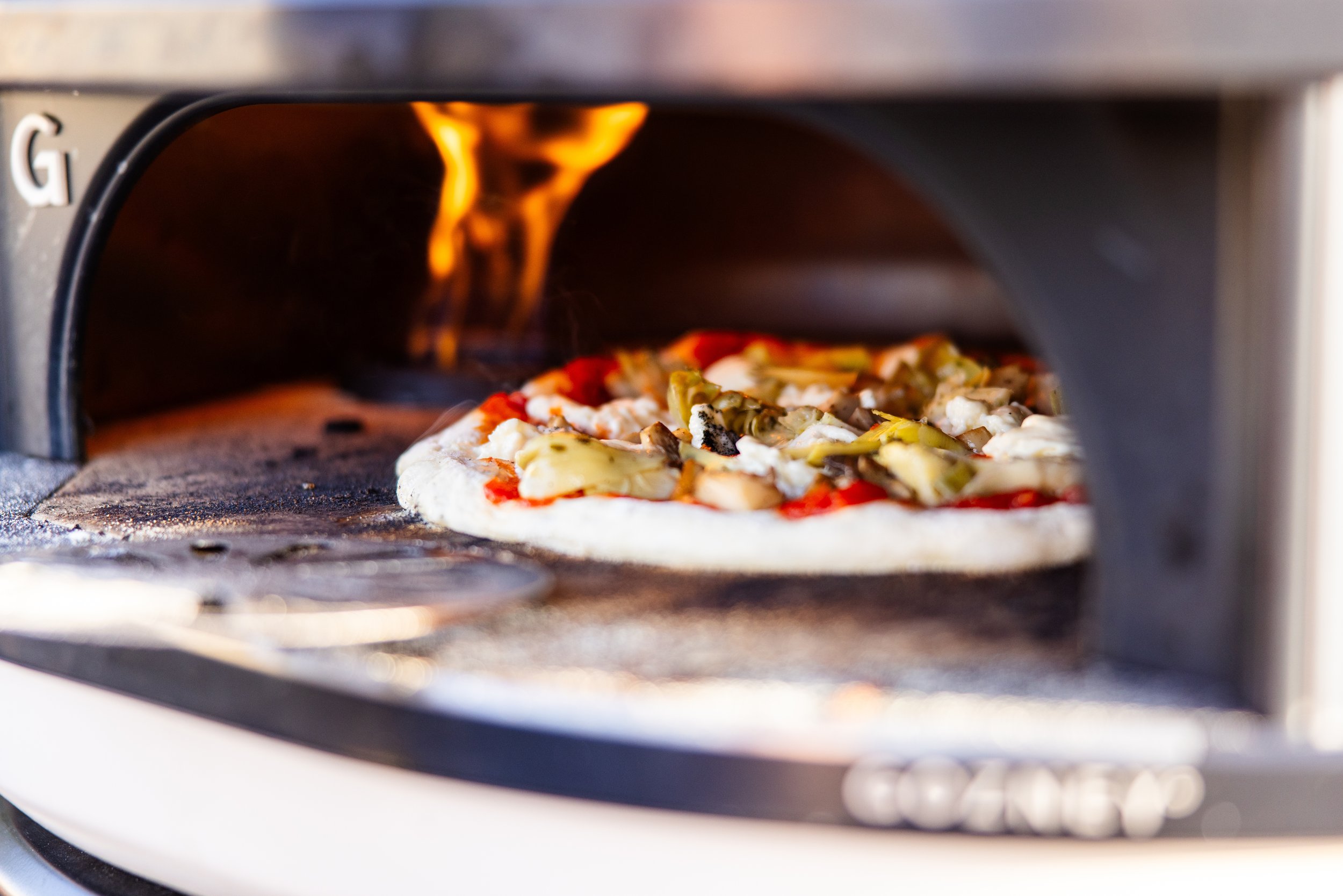 A person baking a pizza on a pellet grill outdoors.
