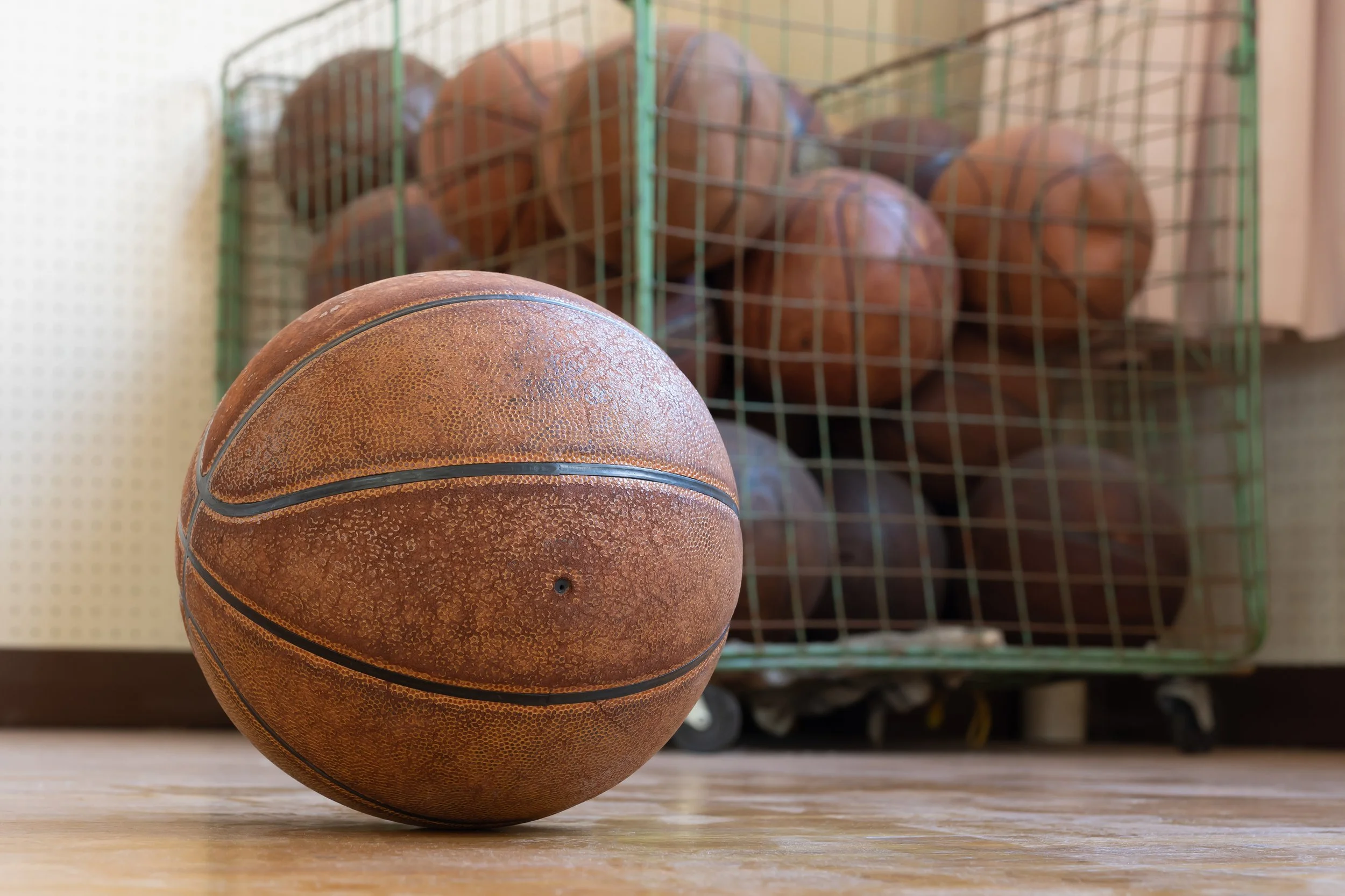 Brukket basketball på gulvet med en kurv med flere basketballer i bakgrunnen.
