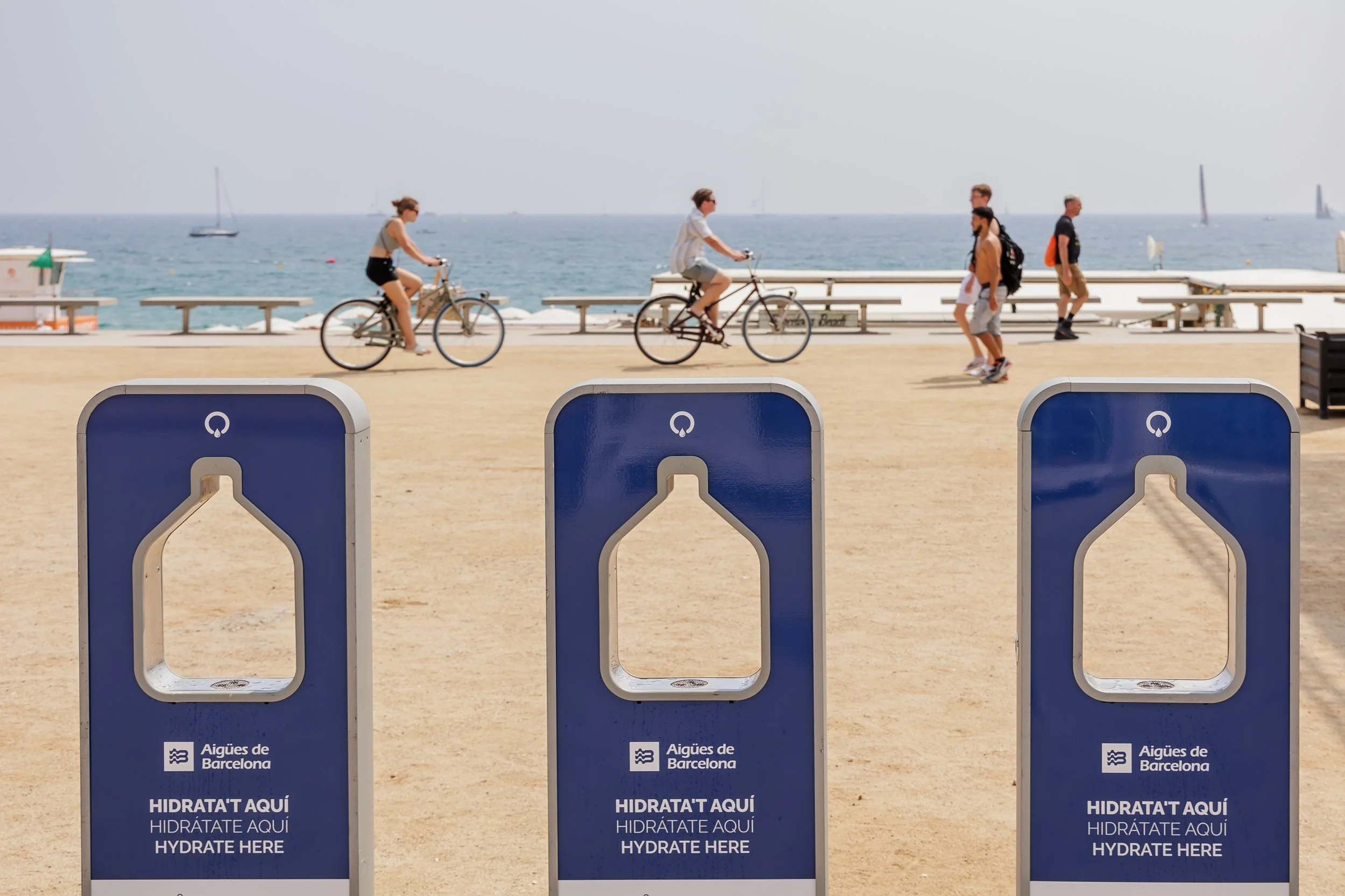 Estaciones de hidratación en la playa de Barcelona con personas paseando y en bicicleta al fondo