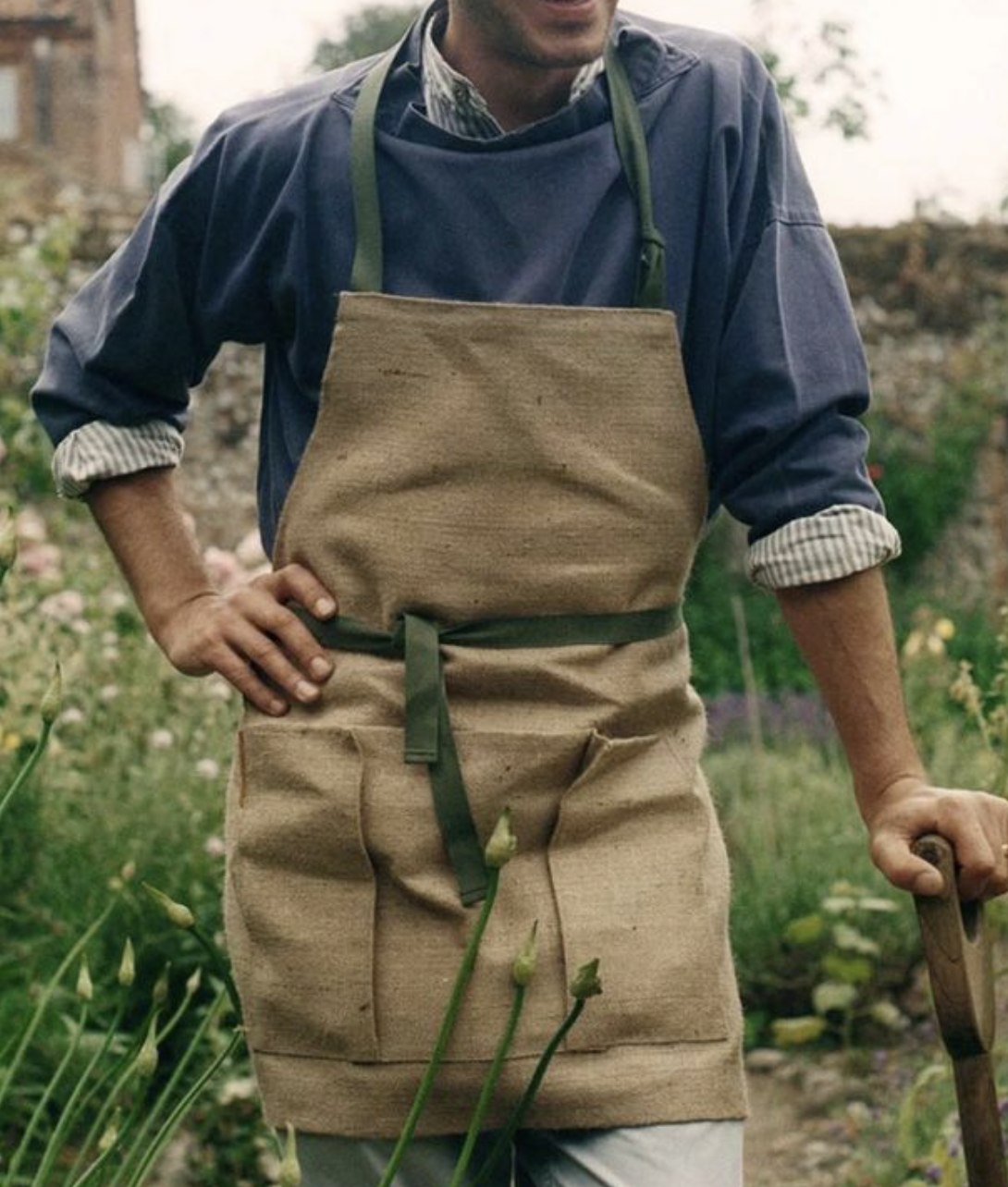 Persona con delantal en un jardín, sosteniendo una herramienta de jardinería.