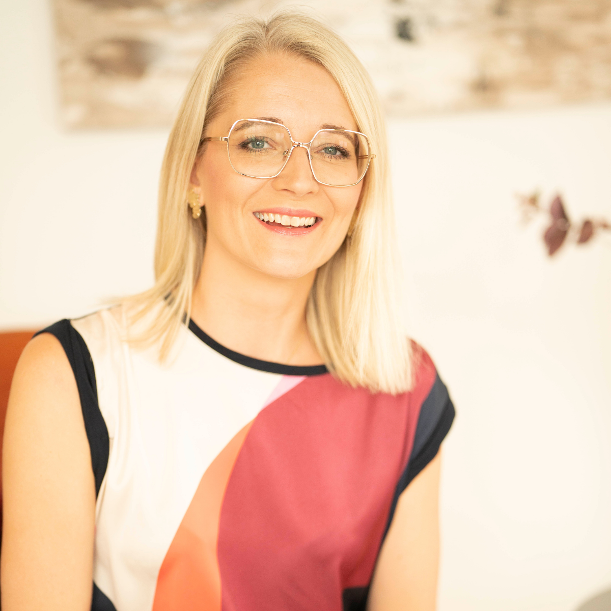 Rikke Lundsfryd, business wingwoman med blondt hår, briller og farverigt tøj, indendørs med neutral baggrund.