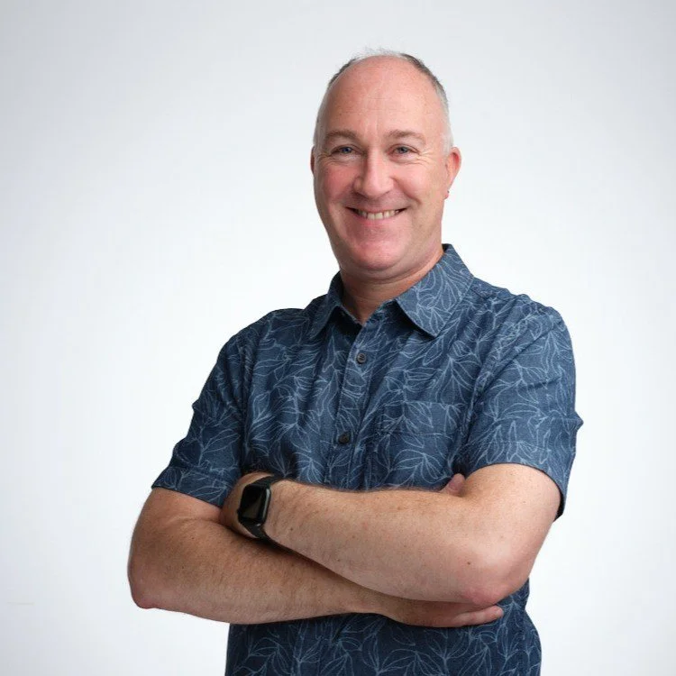 Smiling man with crossed arms wearing a blue patterned shirt and smartwatch.