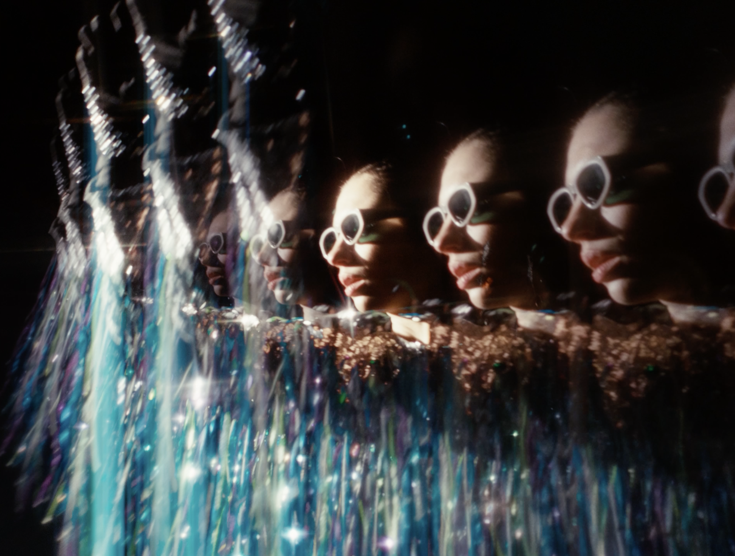 Portrait artistique avec effets kaléidoscopiques d'une personne portant des lunettes de soleil blanches et un vêtement scintillant.